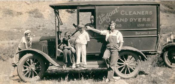 Historical black and white photo of a 1910s open-air delivery truck with four children in front of it, advertising 'Hough Cleaners and Dyers'