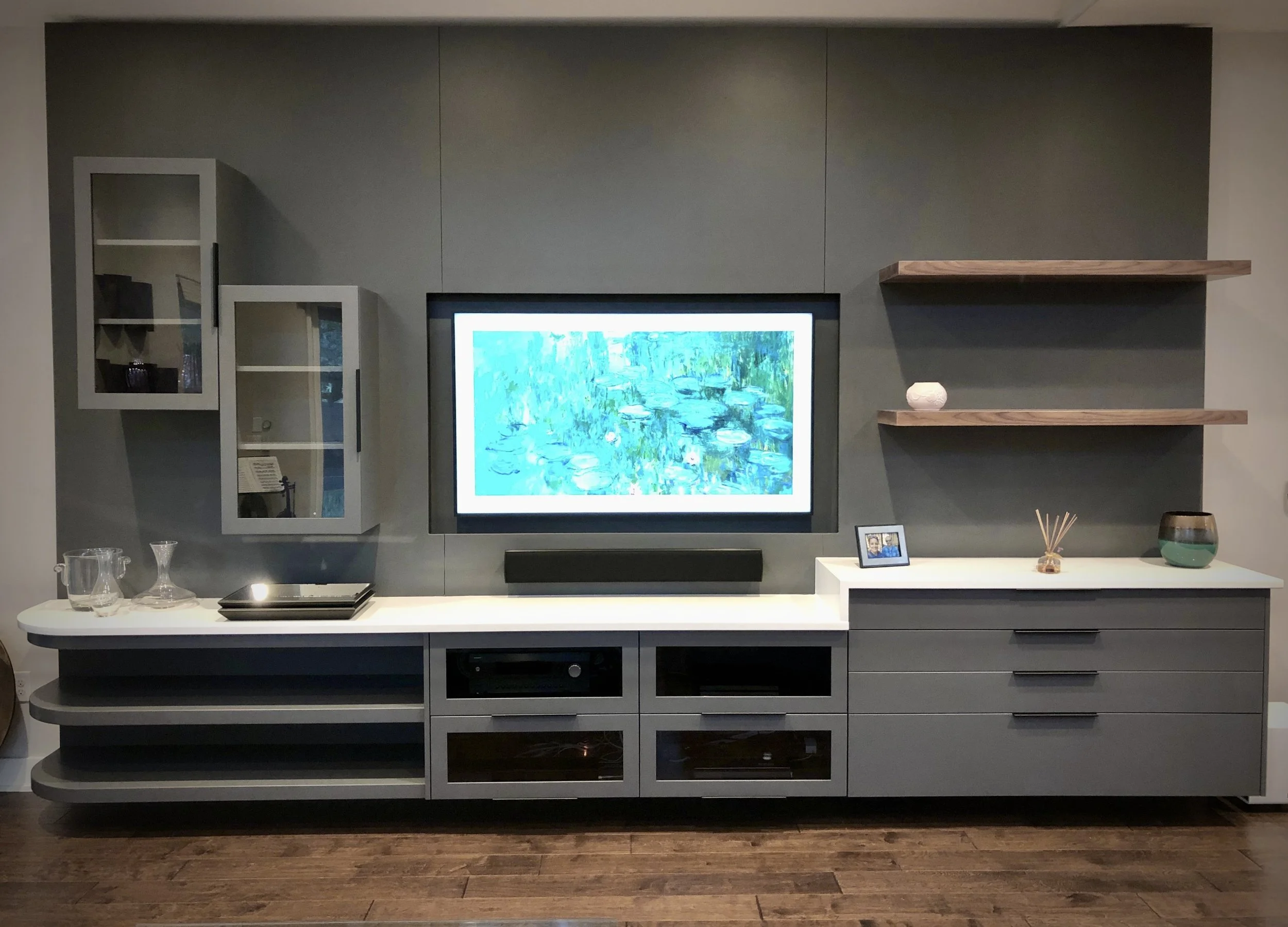Modern living room entertainment unit with a large flat-screen TV displaying a water lily pond scene, surrounded by decorative shelves and glassware.