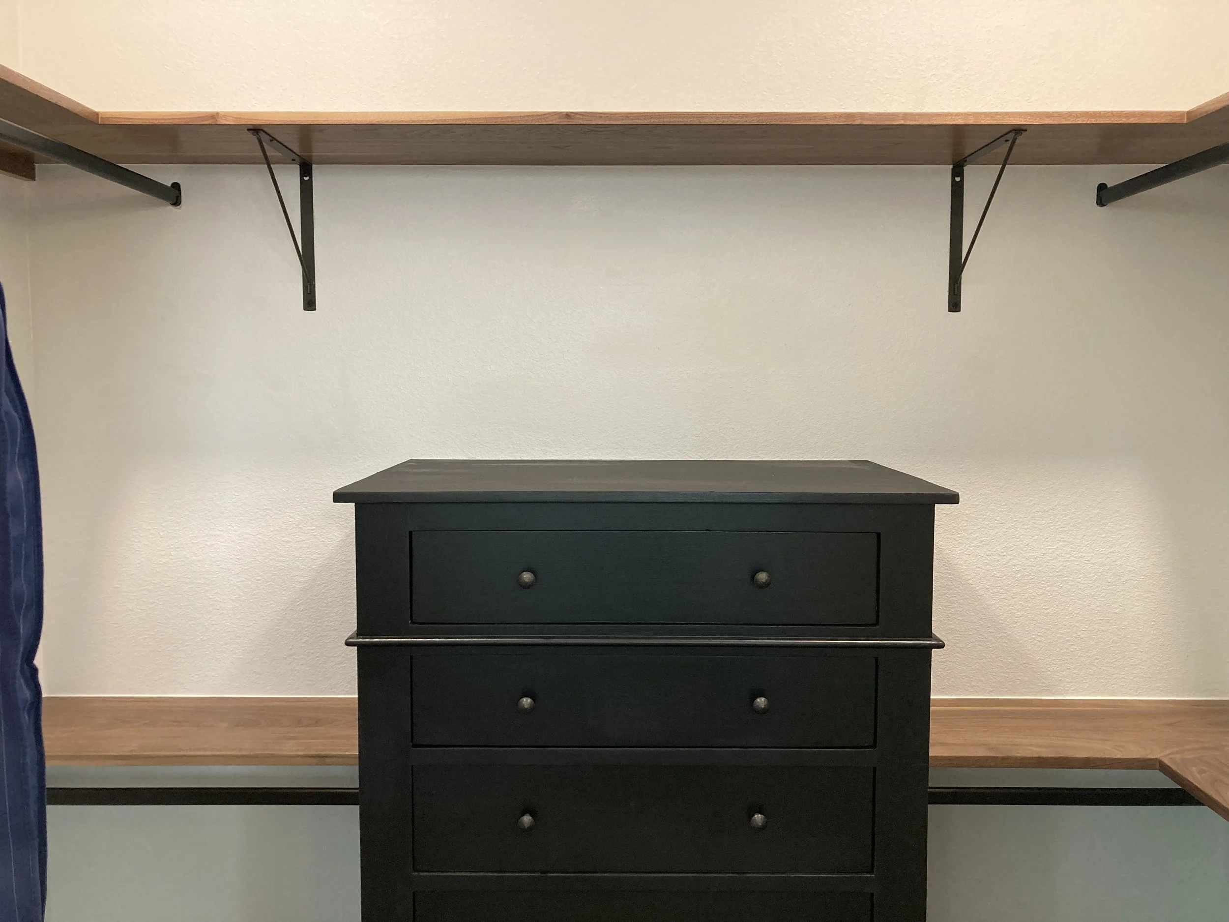 Empty closet with a black dresser and wooden shelves.