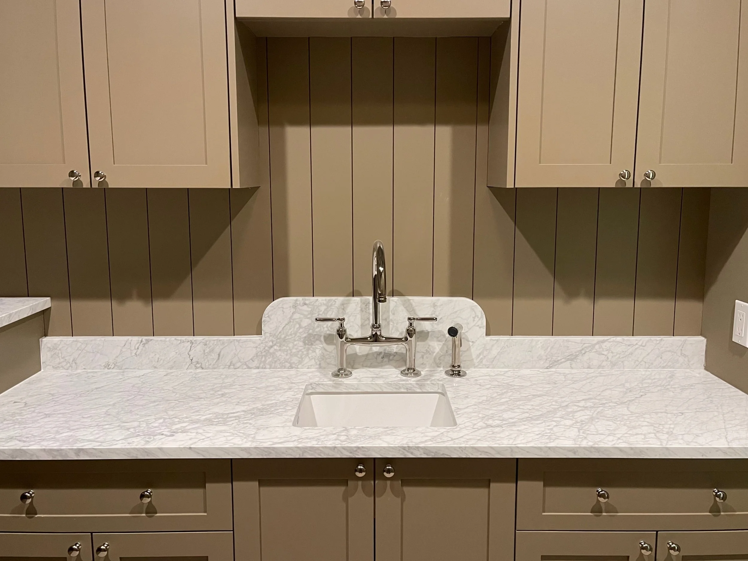 Kitchen sink with marble countertop, faucet, and beige cabinets in the background.