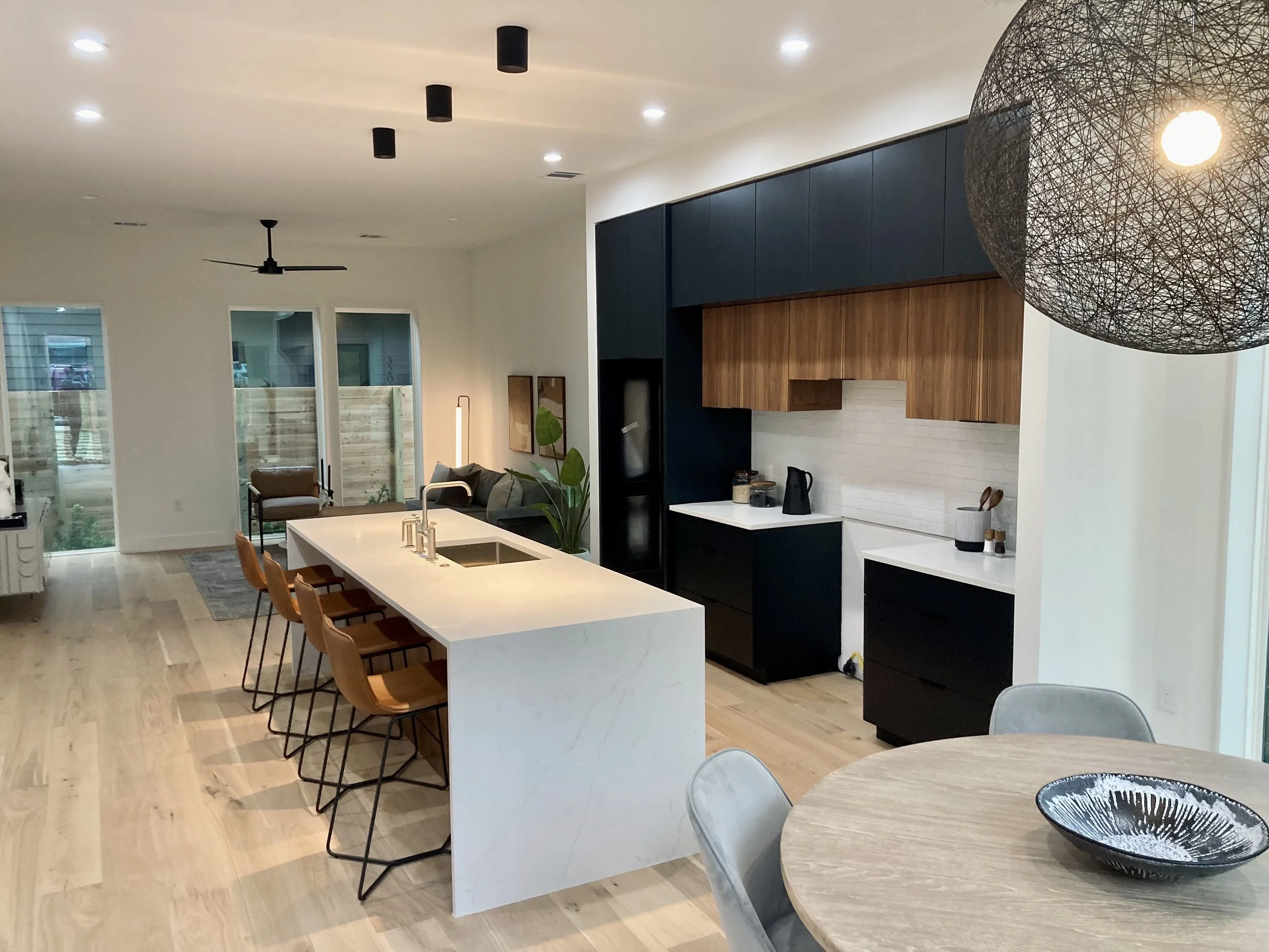 Modern open-concept kitchen and living area with a large white island, black and wood cabinetry, and a round dining table.