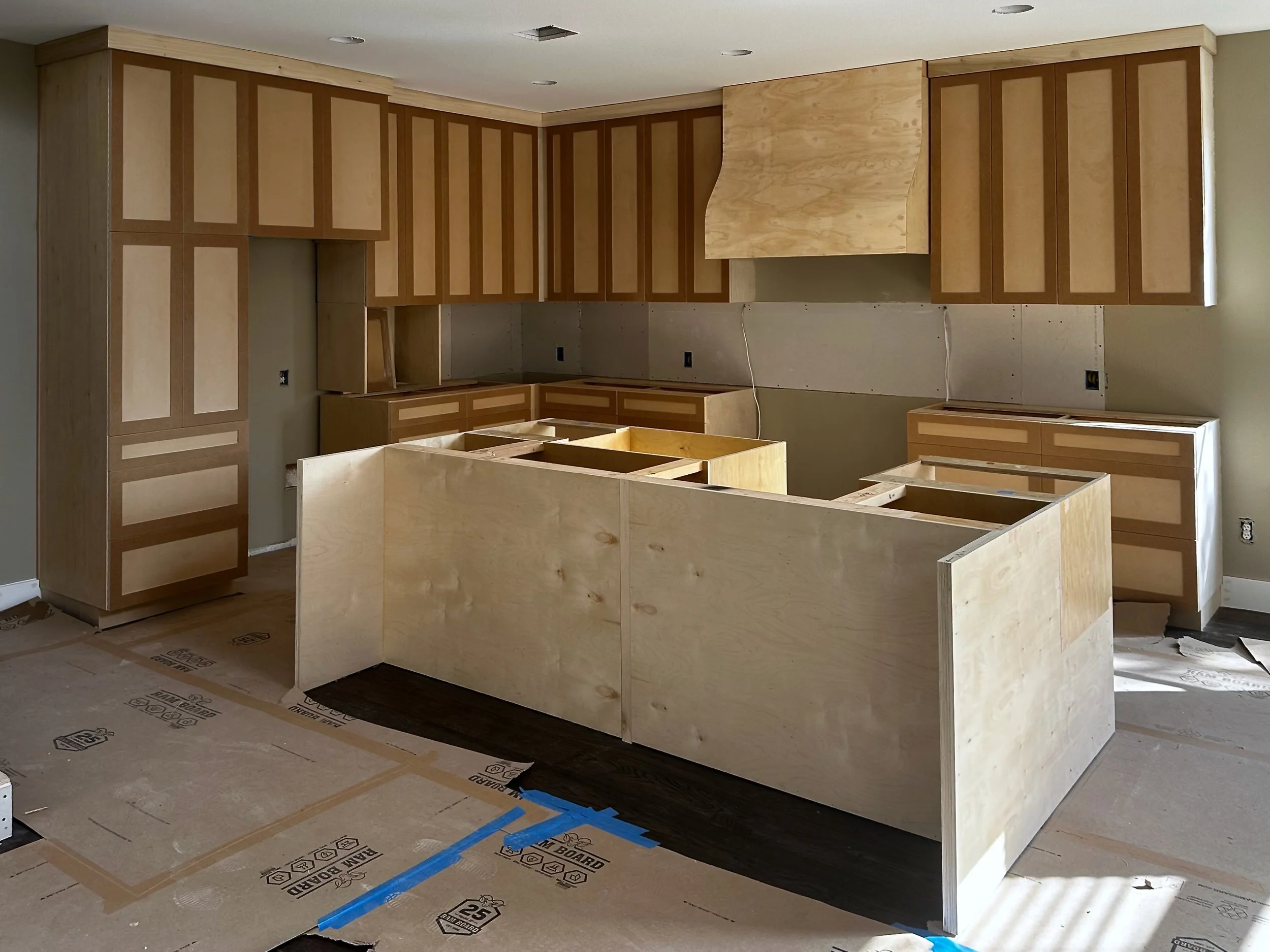 Kitchen under construction with wooden cabinets and countertops being installed.