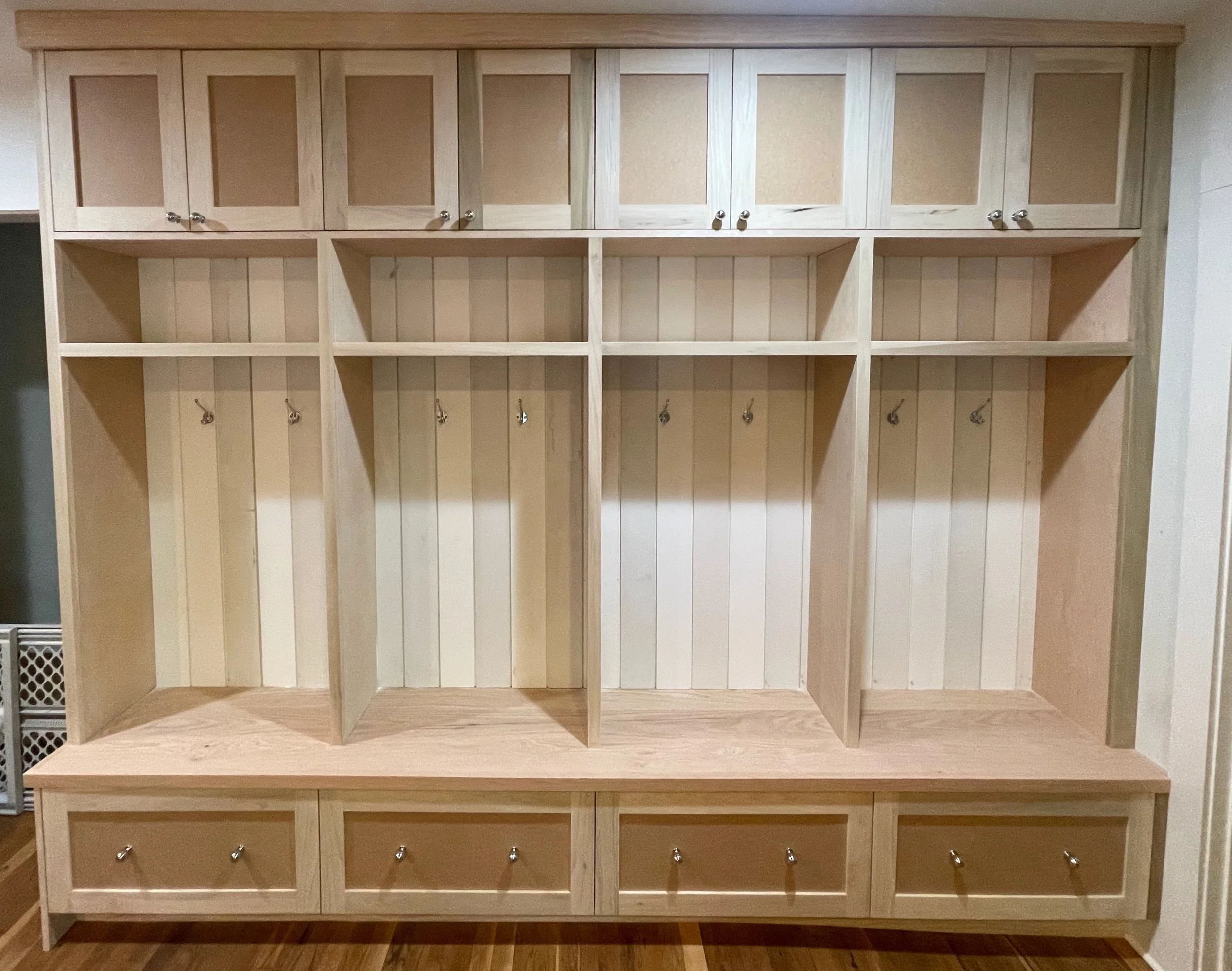 Unfinished wooden coat rack with upper cabinets, open hooks in the middle, and lower drawers.