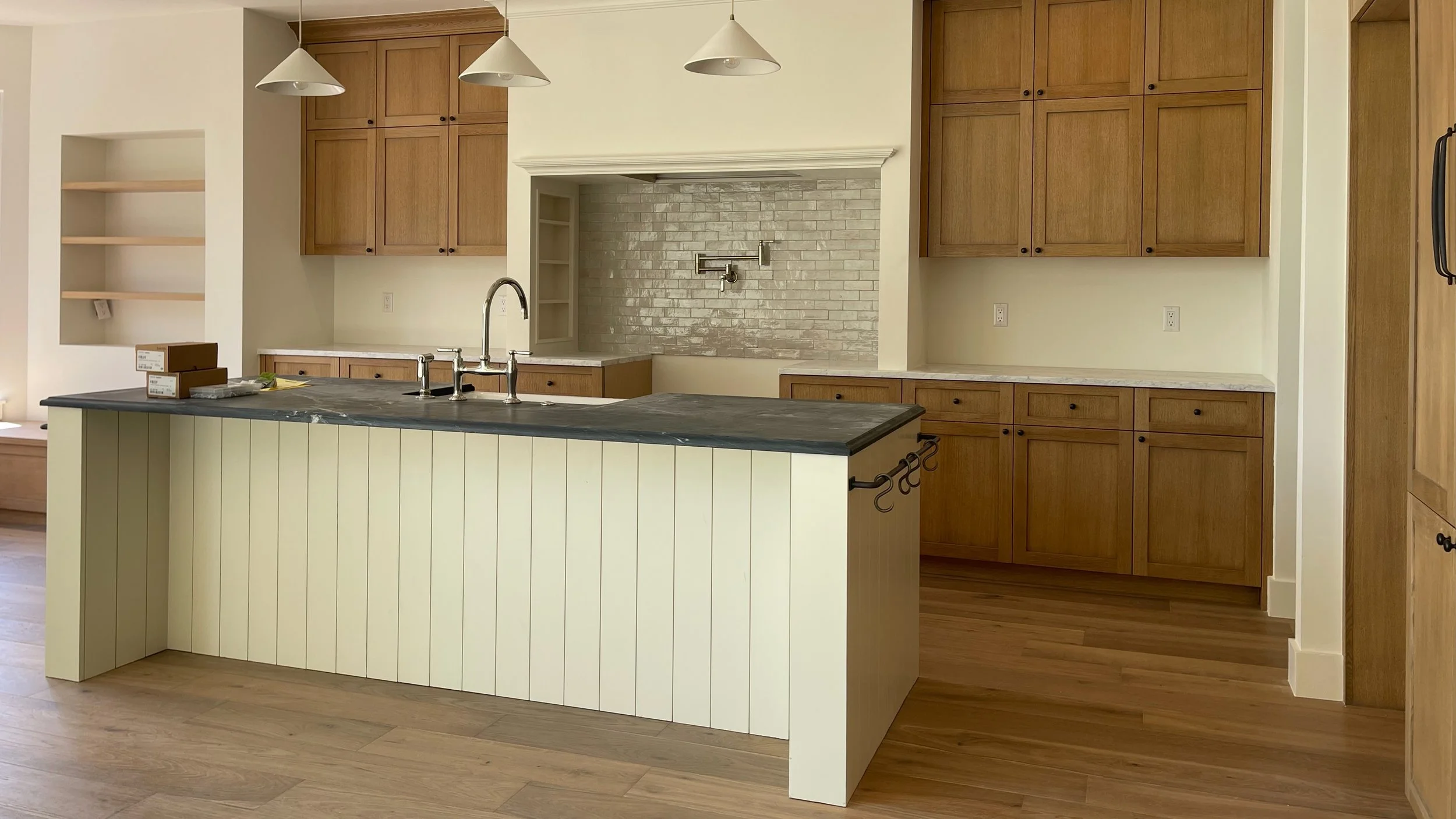 Modern kitchen with wooden cabinets, a black countertop island, a white brick backsplash, and a stainless steel sink and faucet.