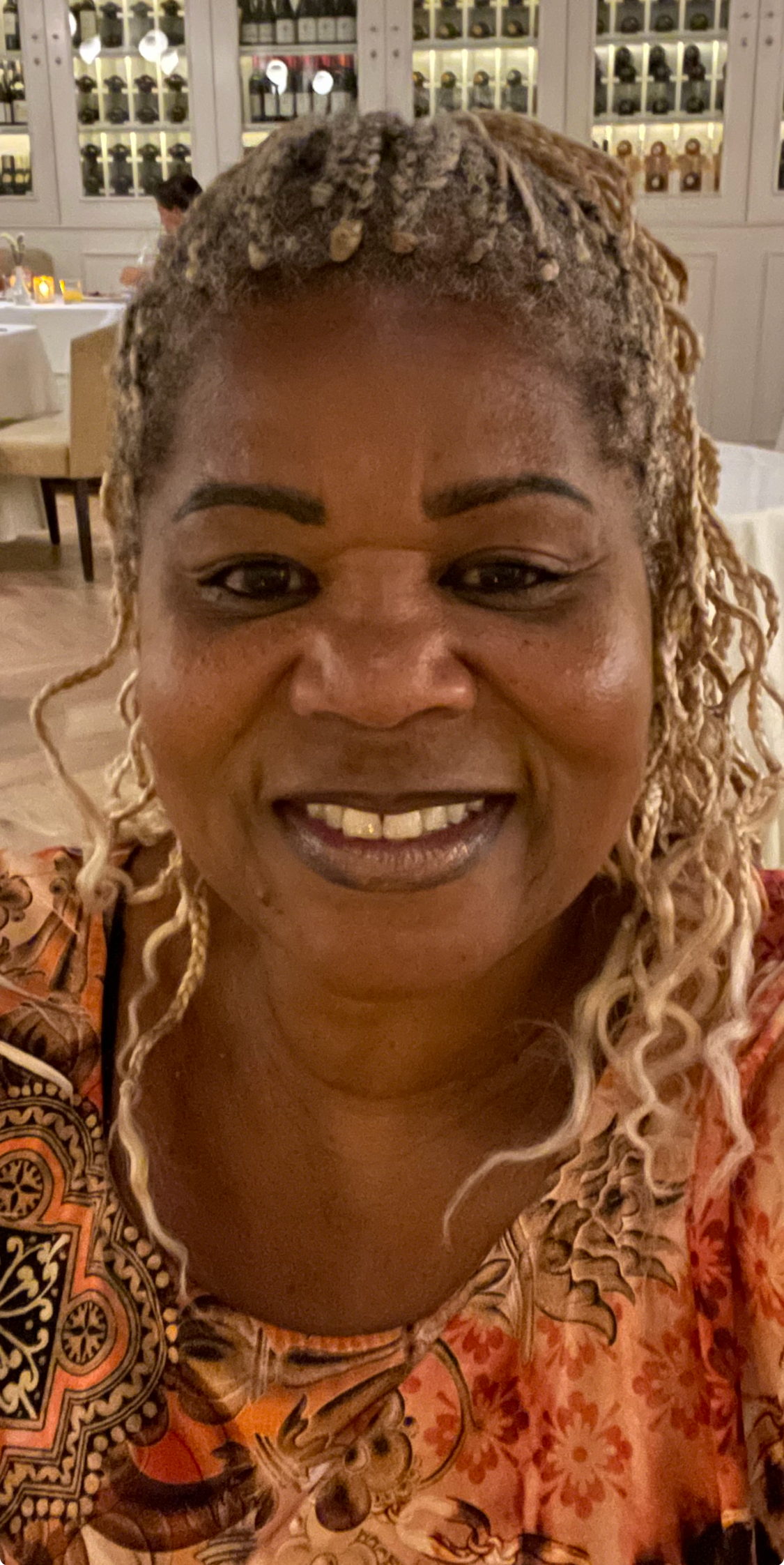 Josephine with blonde dreadlocks wearing a colorful patterned dress, smiling.