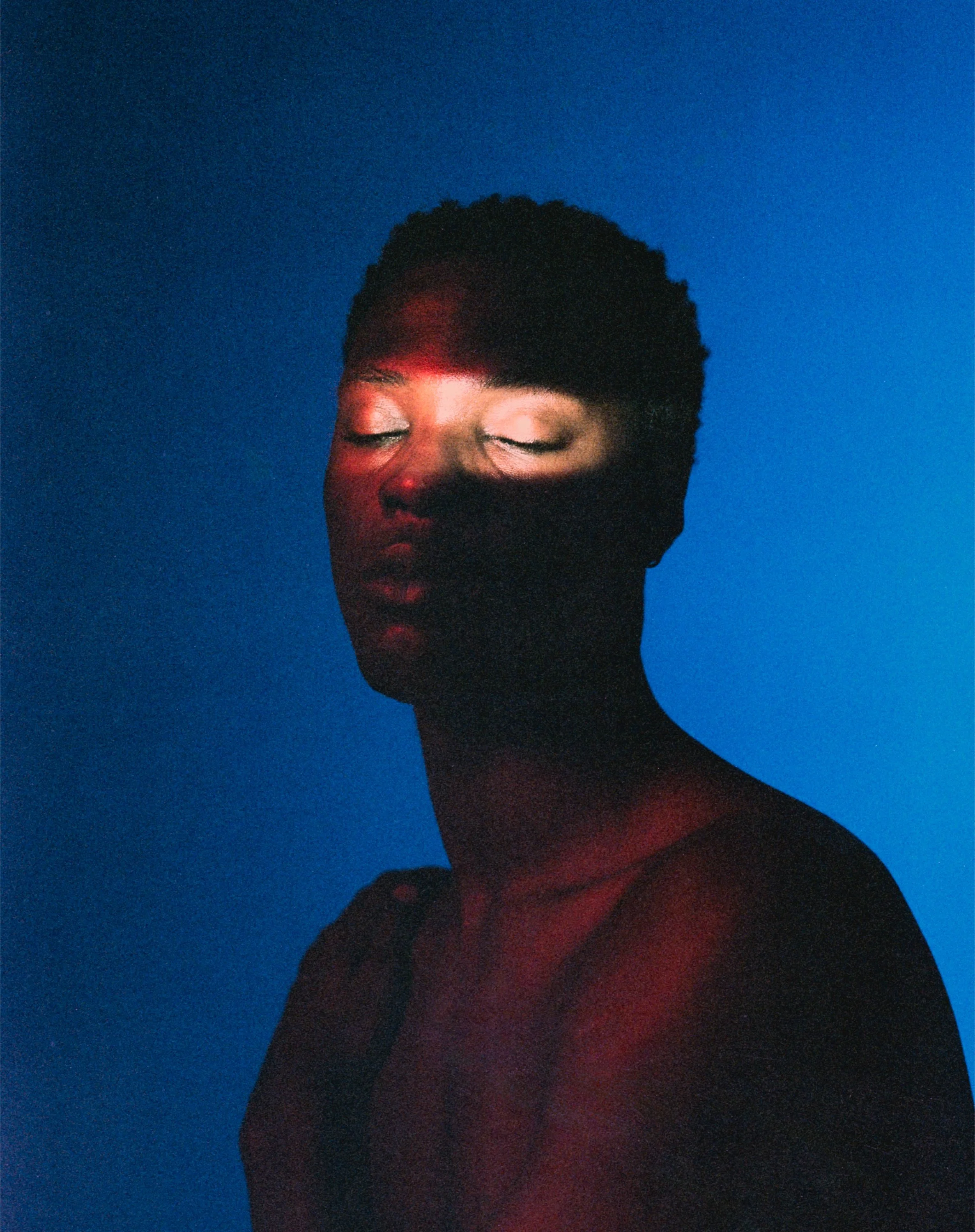 Portrait of a woman with closed eyes, illuminated by red and white light, against a blue background.
