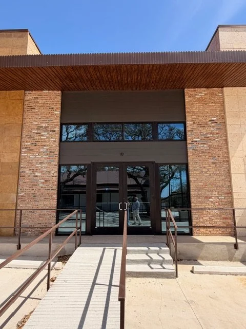 Front entrance of a modern building with brick and concrete walls, glass doors, and a ramp for accessibility.
