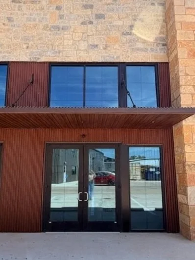 Front view of a building with large glass doors and windows, featuring brick and wood exterior walls.