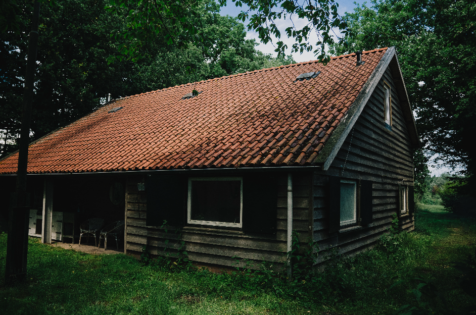 Een houten huis met een rode dakpan bedekte dak, omringd door groene bomen en gras.