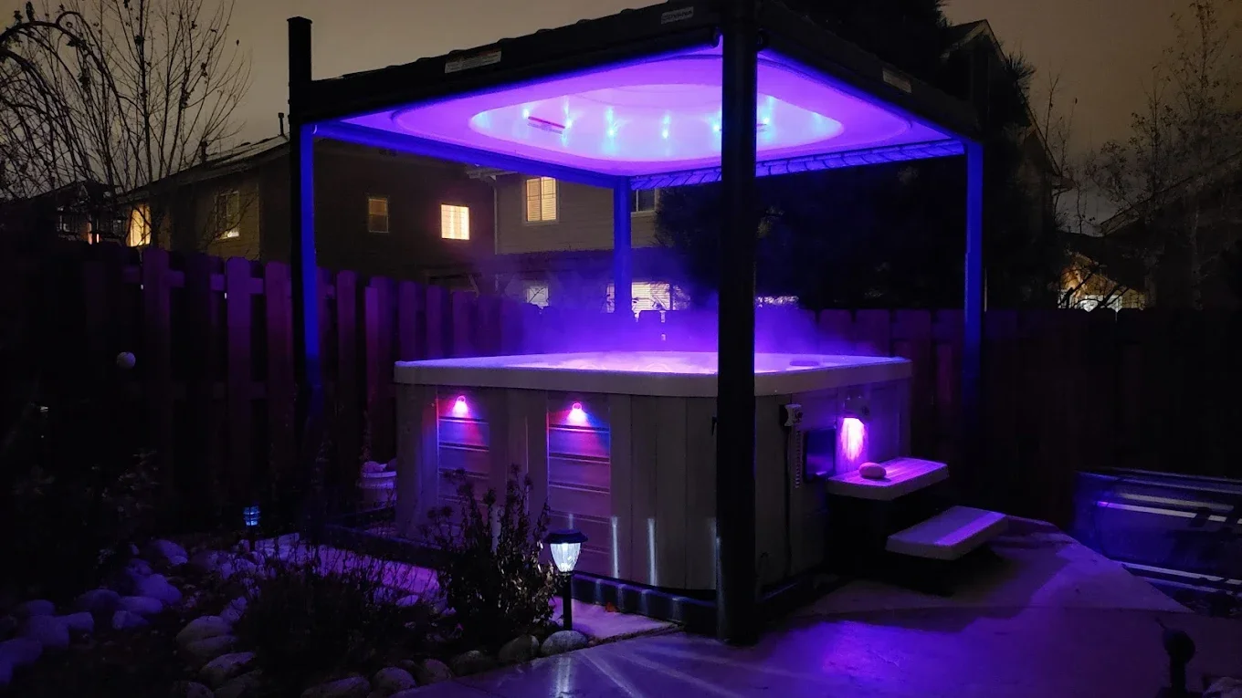 Illuminated hot tub with purple lights in a backyard at night.