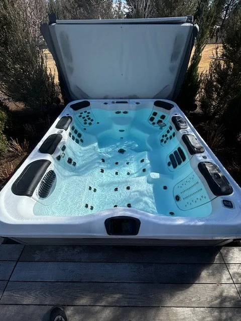Outdoor hot tub with multiple water jets and seating areas, partially covered by a lid.