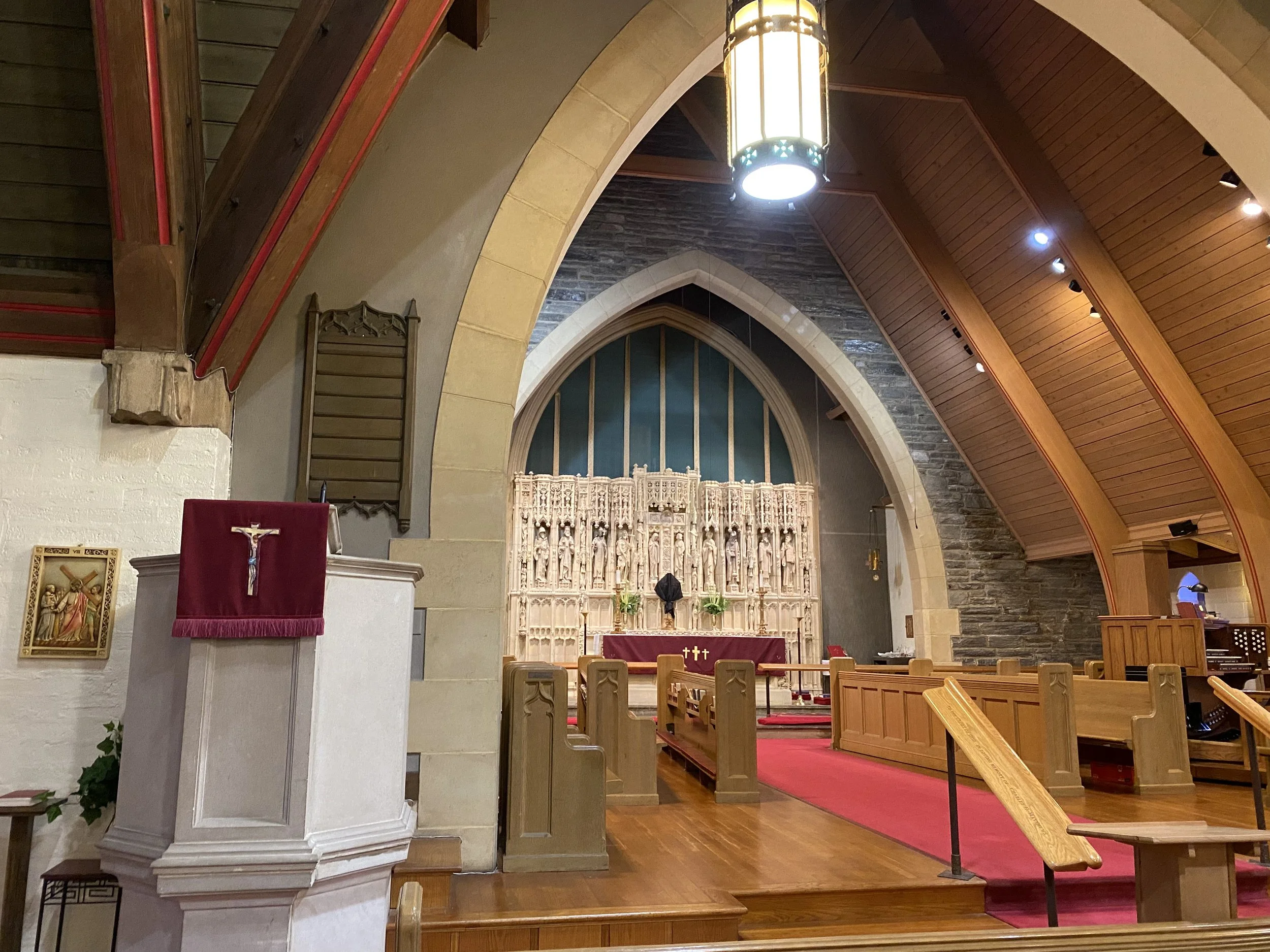 Interior of a church with wooden pews, an altar with religious sculptures, a red carpet, and gothic-style arches.