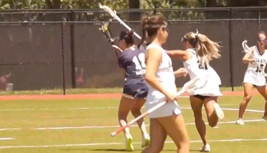 Lacrosse players in white and purple uniforms playing on a field.