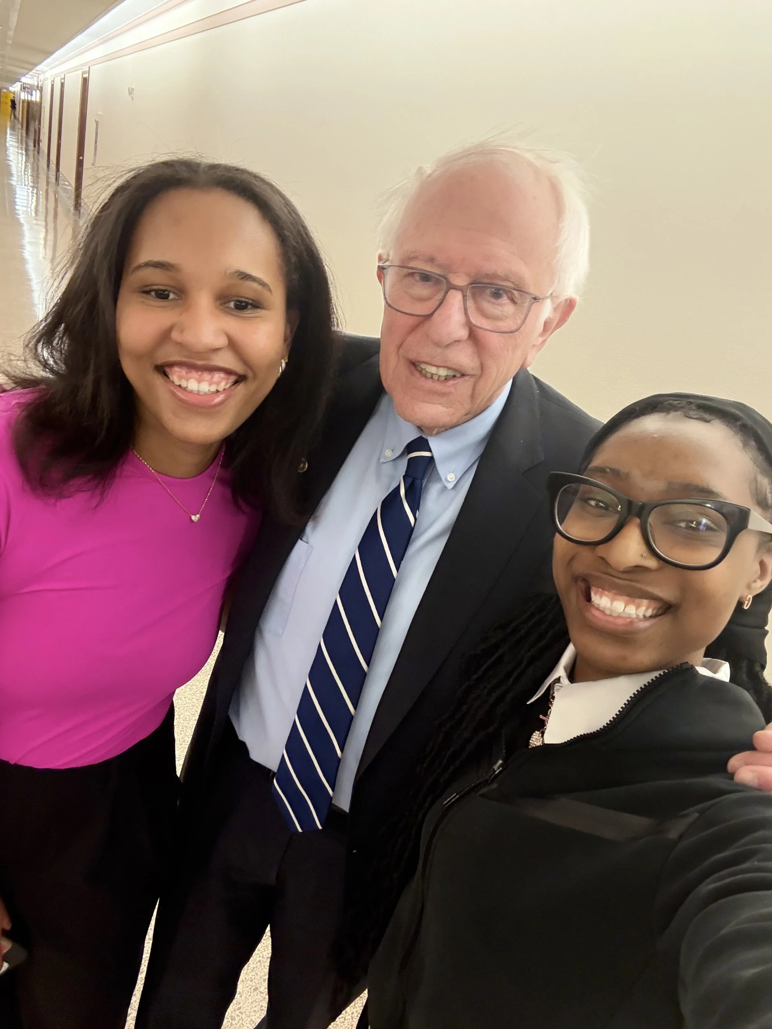 Three people taking a selfie in a hallway, smiling and dressed in formal and casual attire.