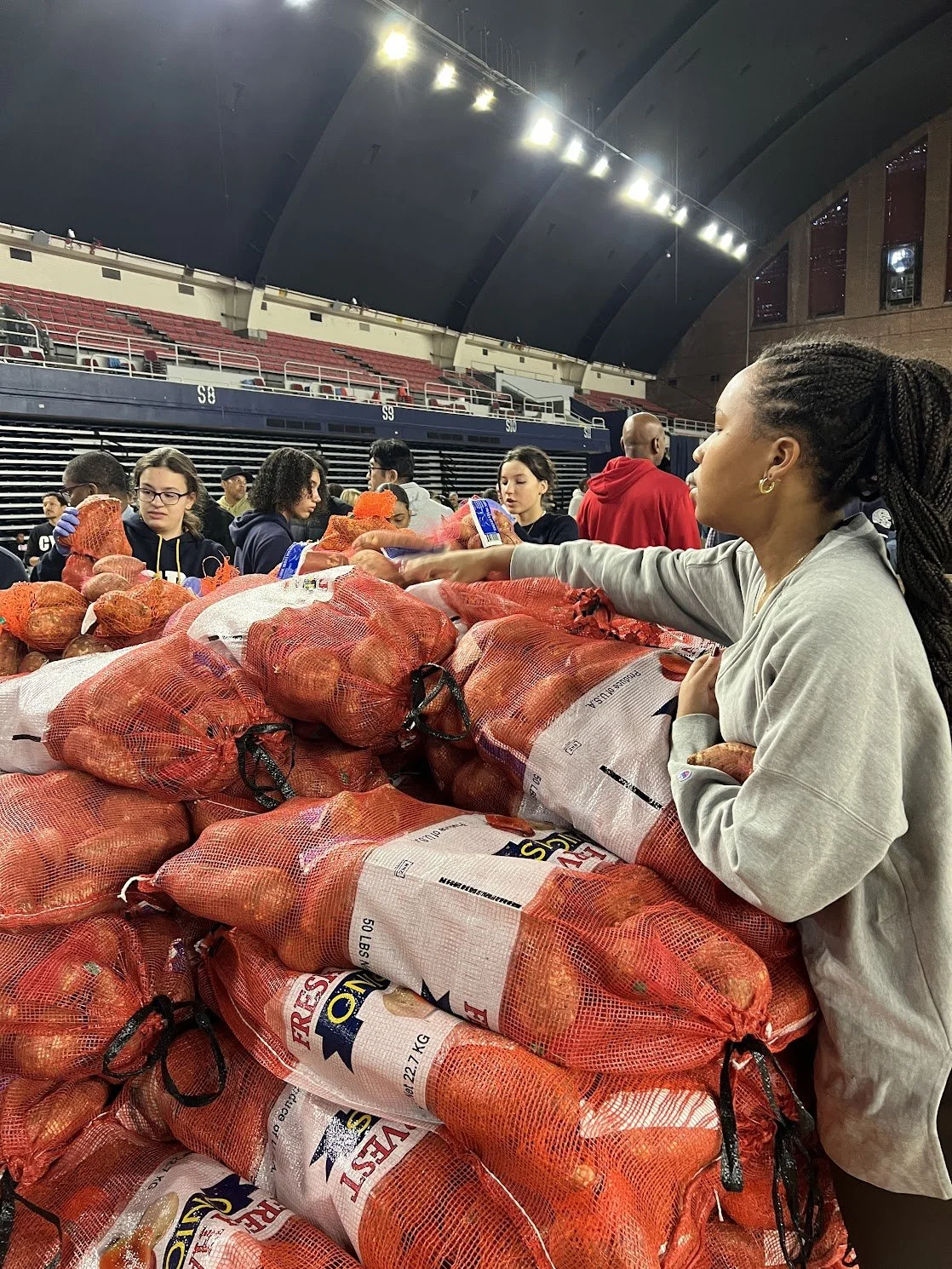 People distributing bags of onions at a community event inside a large indoor stadium.