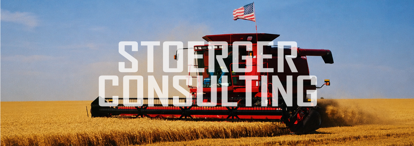 Agricultural combine harvester in a wheat field with an American flag on top, Overlay says STOERGER CONSULTING.