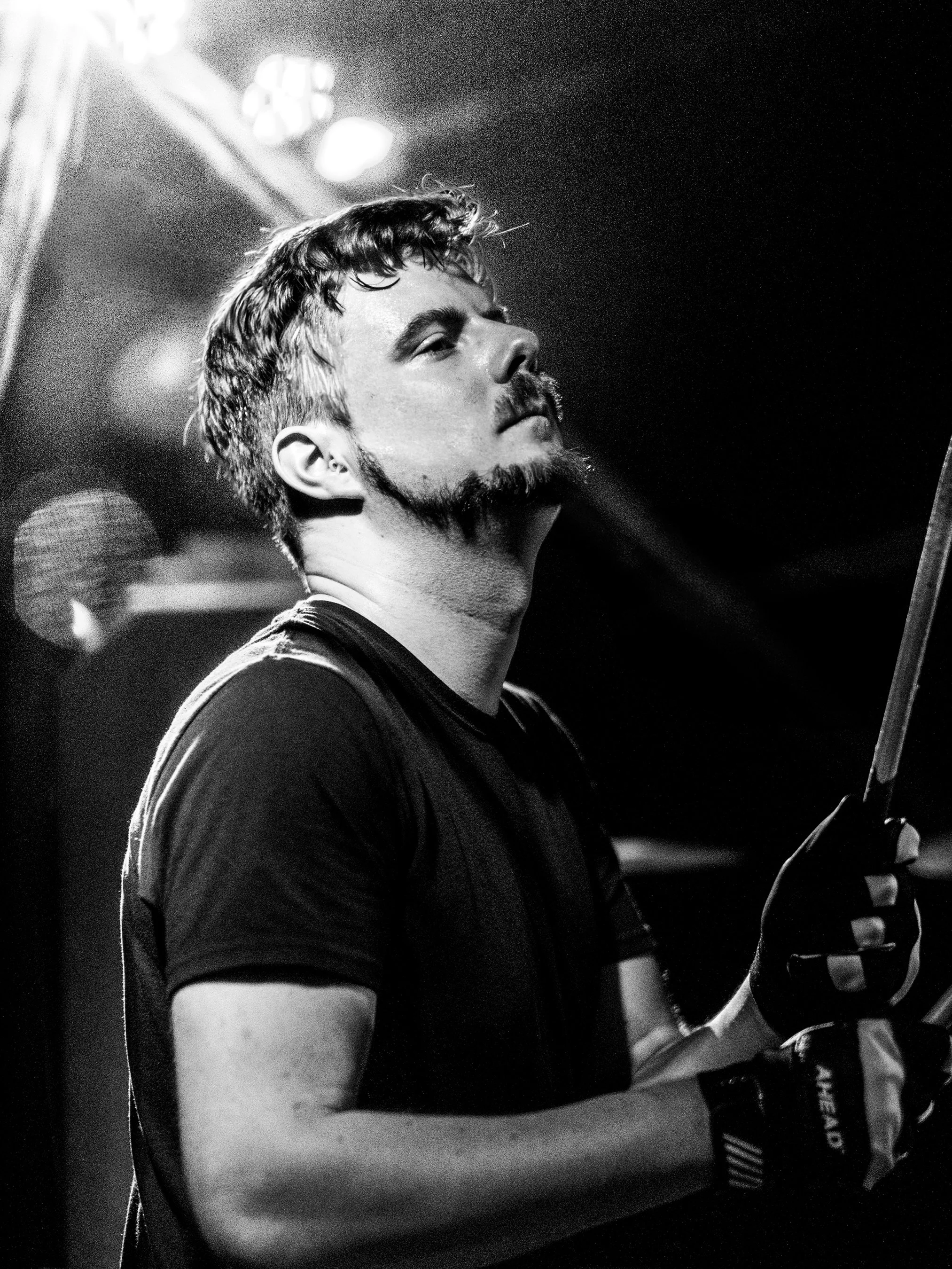 Black and white photo of a man with a beard and mustache, playing the drums.