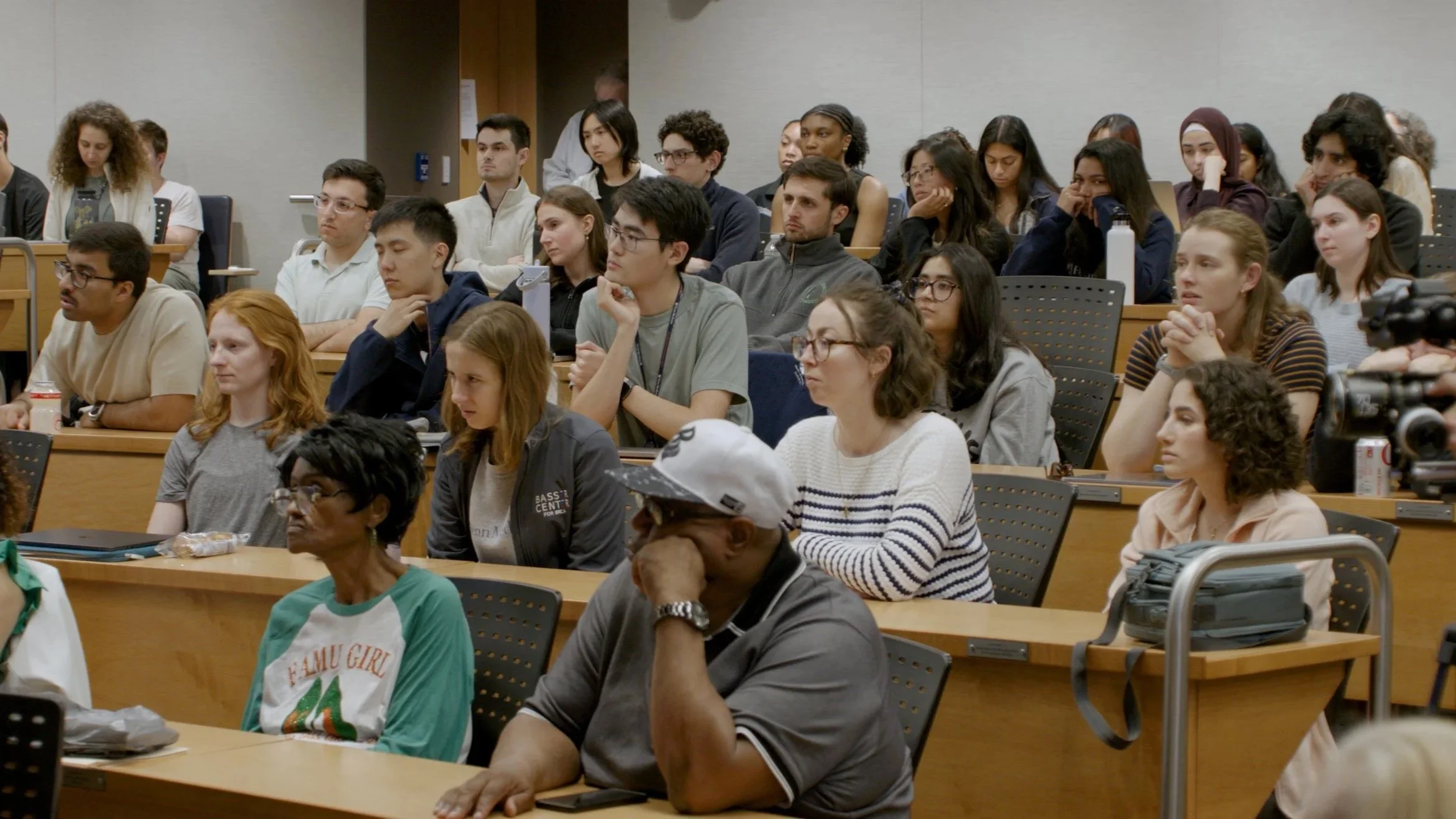 A diverse group of people sitting in an auditorium or lecture hall, attentively listening to a presentation.