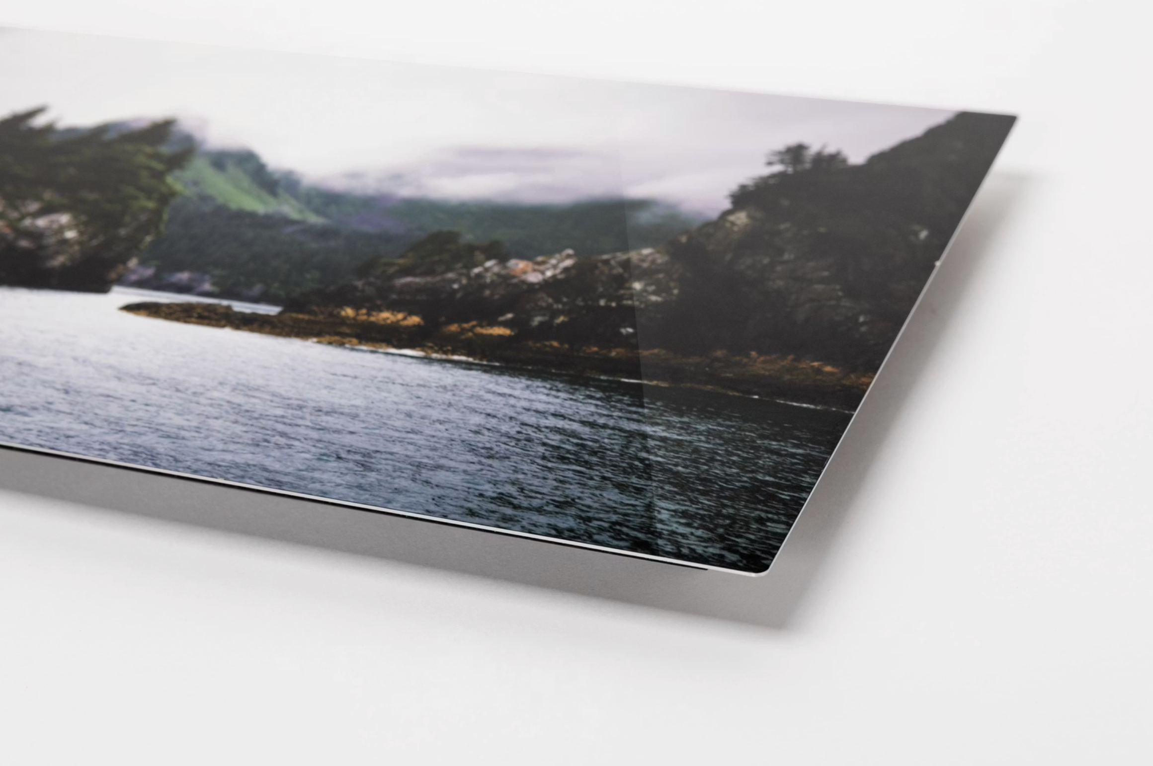 Close-up of a printed photograph showing a coastal landscape with mountains, trees, and water, partially visible on a white surface.