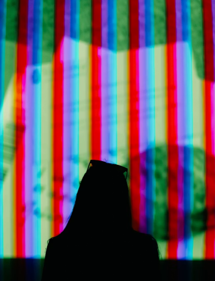 Silhouette of a person with glasses in front of a colorful, distorted digital screen.