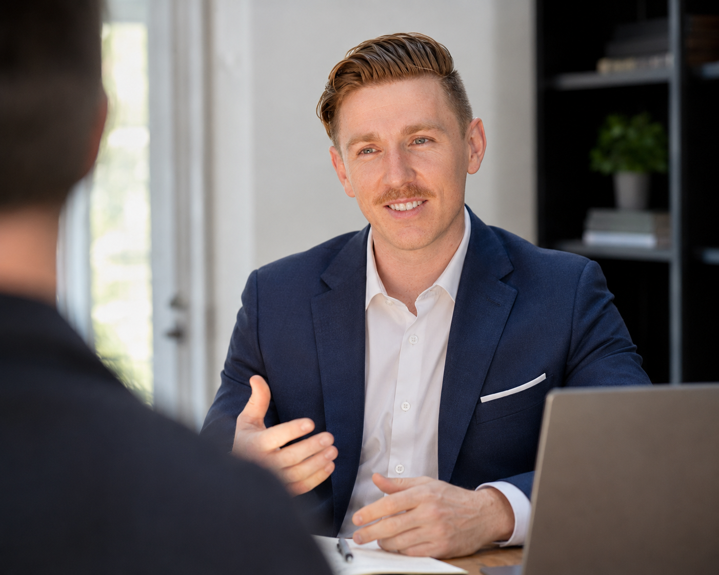 Taylor Hetherington in a blue suit and white shirt smiling during a conversation in an office setting.