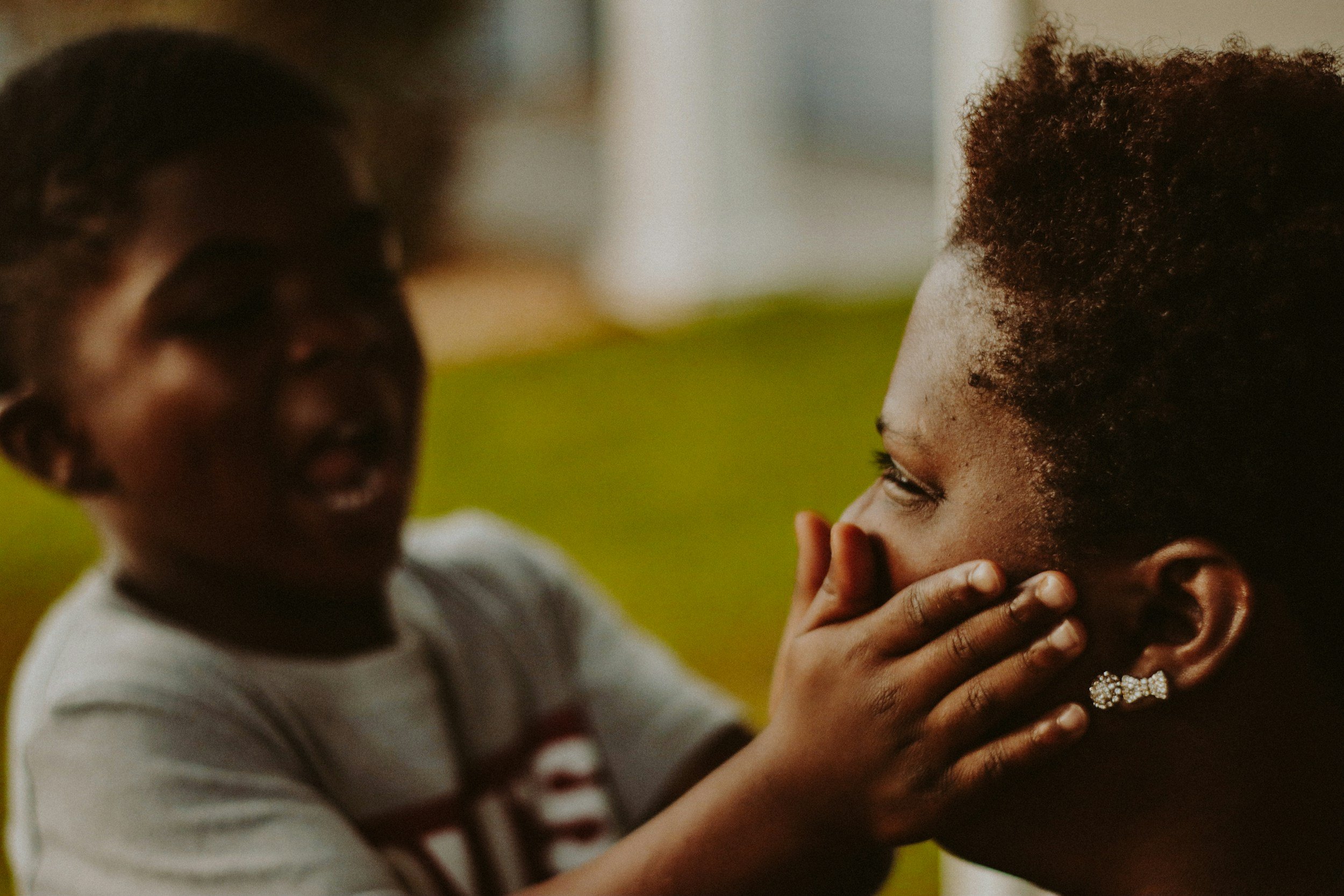 A young child with curly hair gently holds the face of an older woman with curly hair, in a warm, intimate moment.