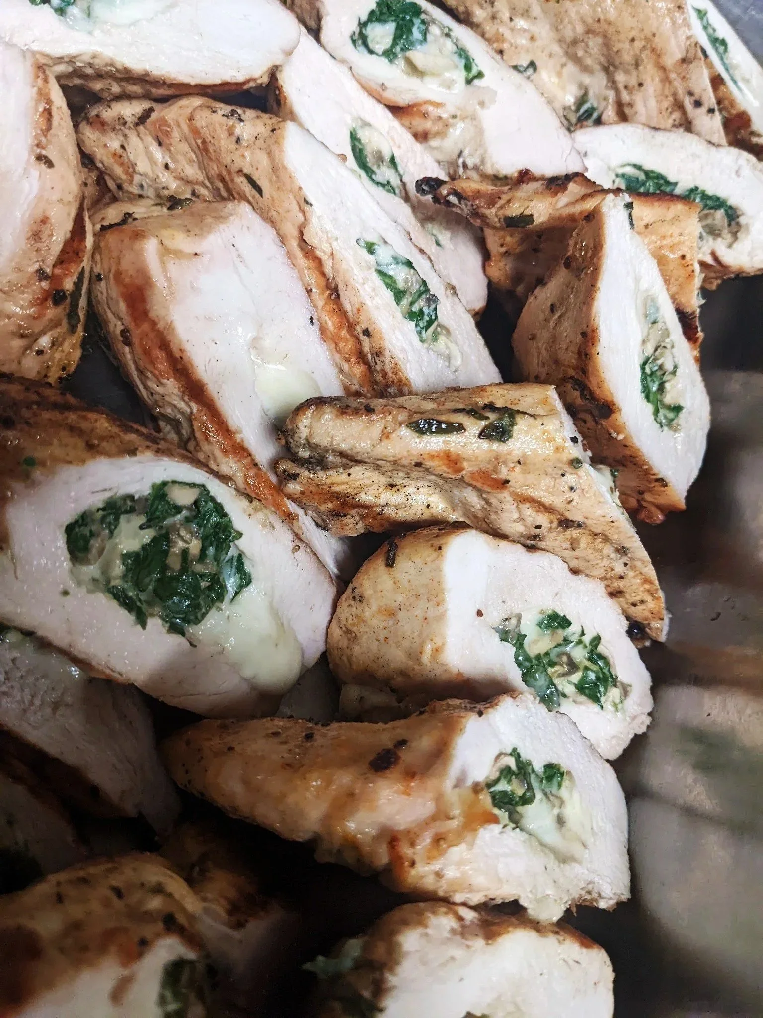 Close-up of cooked chicken breast slices stuffed with herbs and cheese, garnished with chopped green herbs.