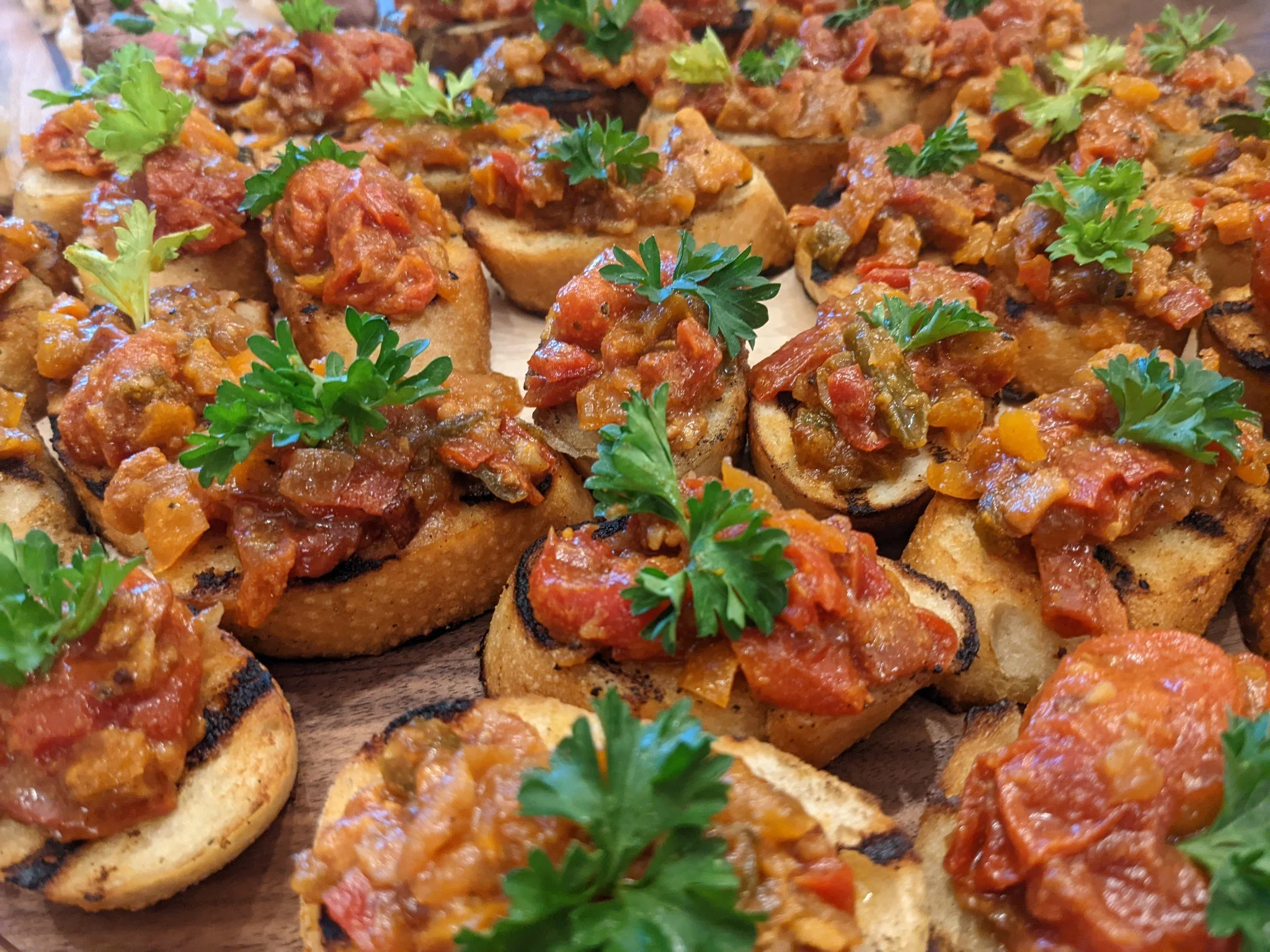 Close-up of toasted bread slices topped with a chunky, red tomato-based vegetable mixture, garnished with fresh parsley leaves.