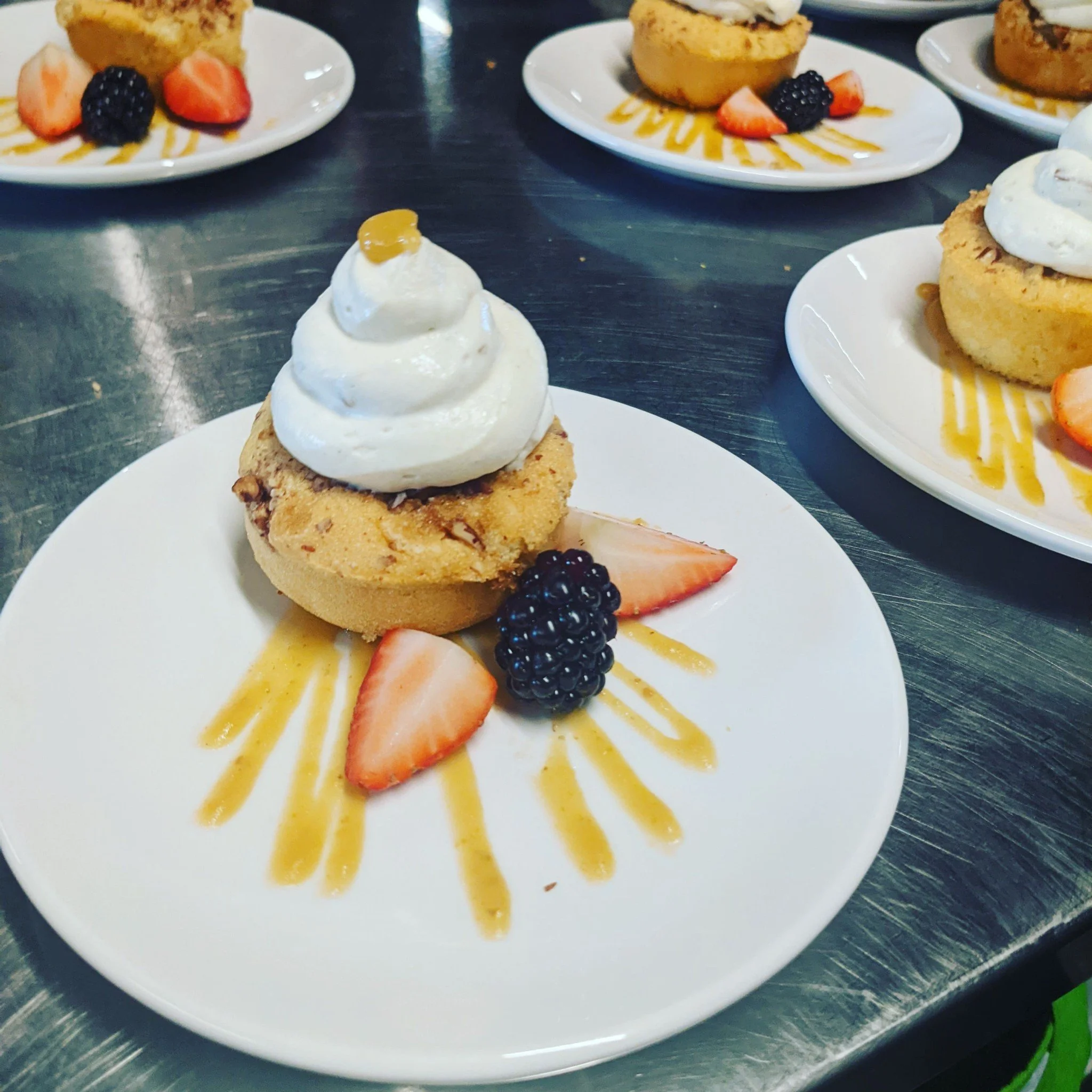 Three plates with desserts and fresh fruit, including strawberries, blackberries, and raspberries, garnished with caramel sauce, and a cupcake with white frosting and a small dollop of caramel on top.