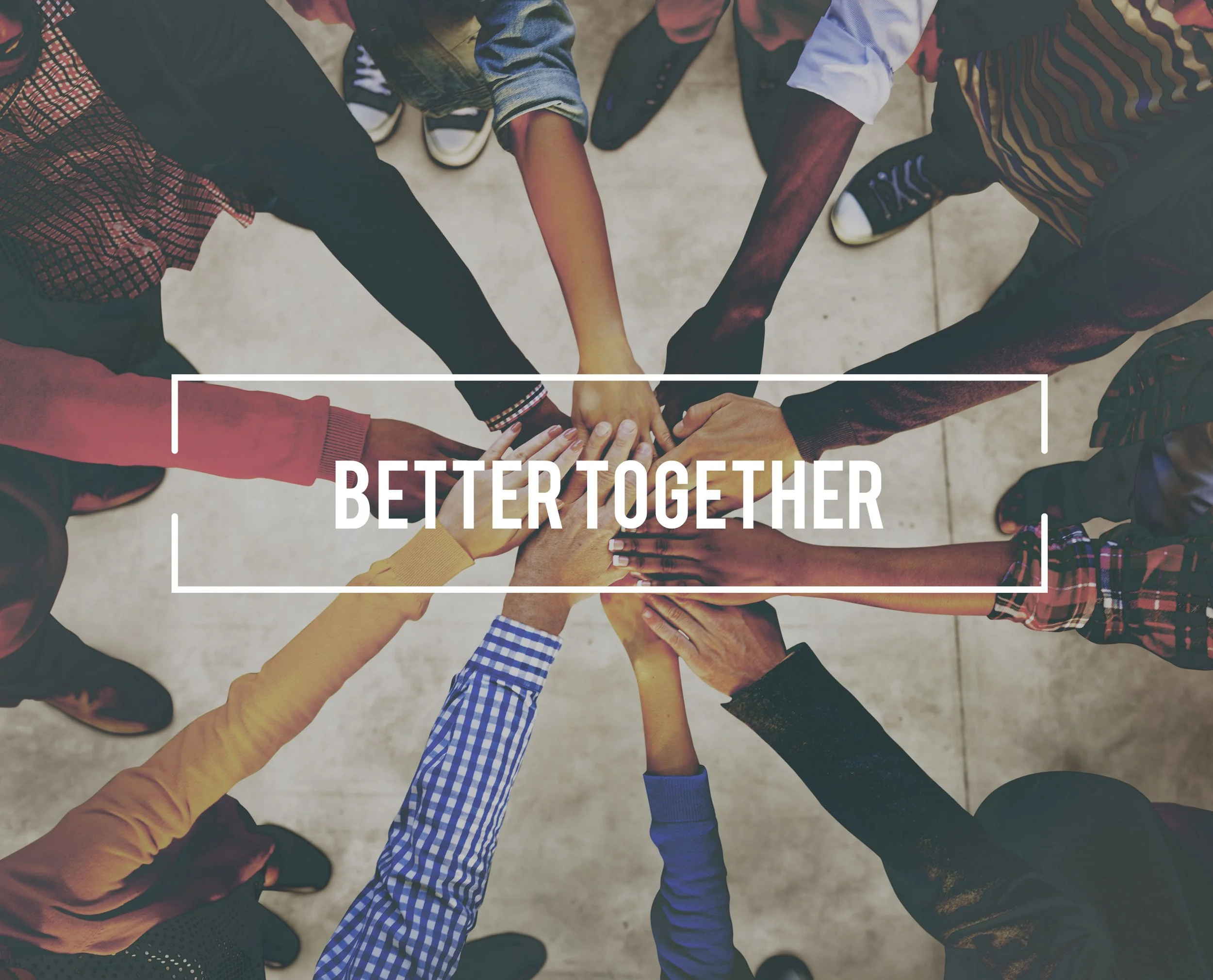 Group of diverse people in casual attire forming a circle with their hands stacked in the center.