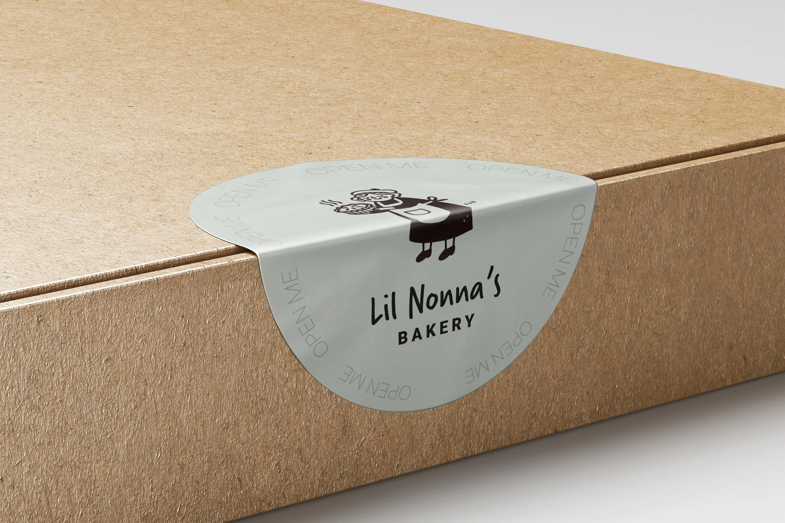 Close-up of a light brown bakery box with a circular sticker that has a cartoon baker illustration and text for Lil Nonna's Bakery.
