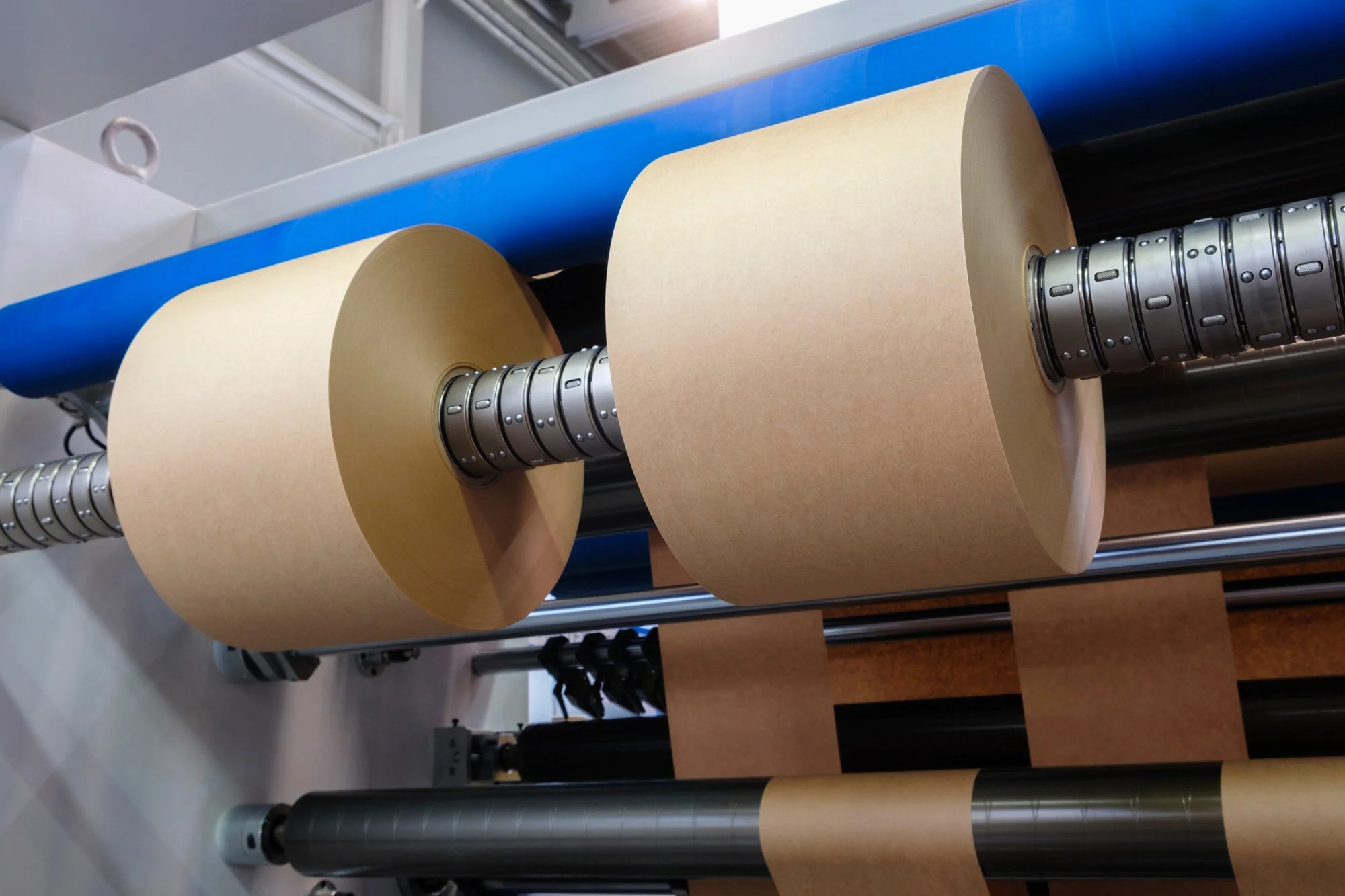 Close-up of industrial rollers with beige paper rolls, metallic and black parts in a machinery setup.