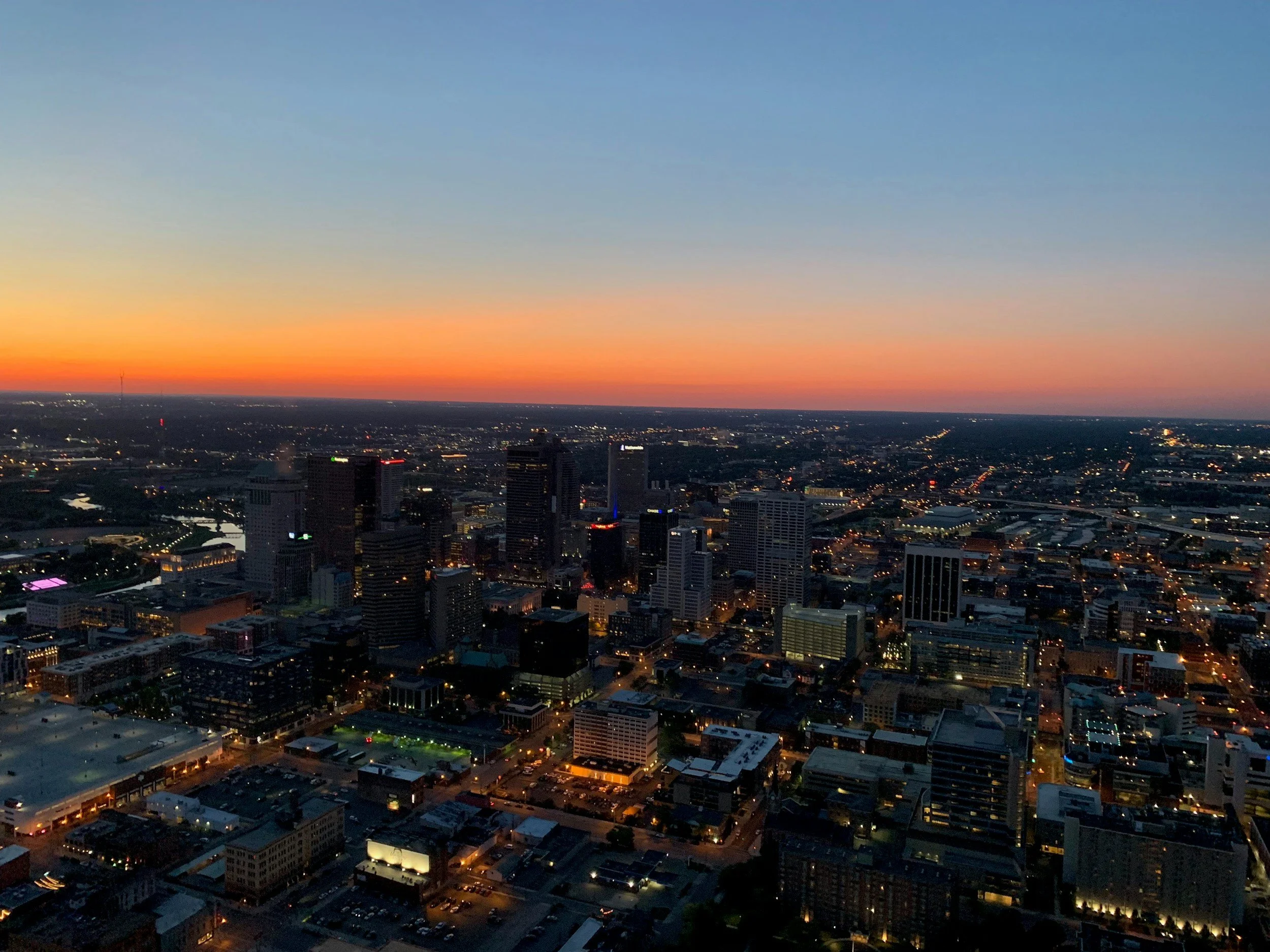 Aerial view of the downtown Columbus, Ohio skyline at sunset with city lights and orange evening sky.