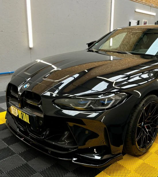 Voiture BMW noire avec un cache-plaques 'Keep Official' dans un garage.
