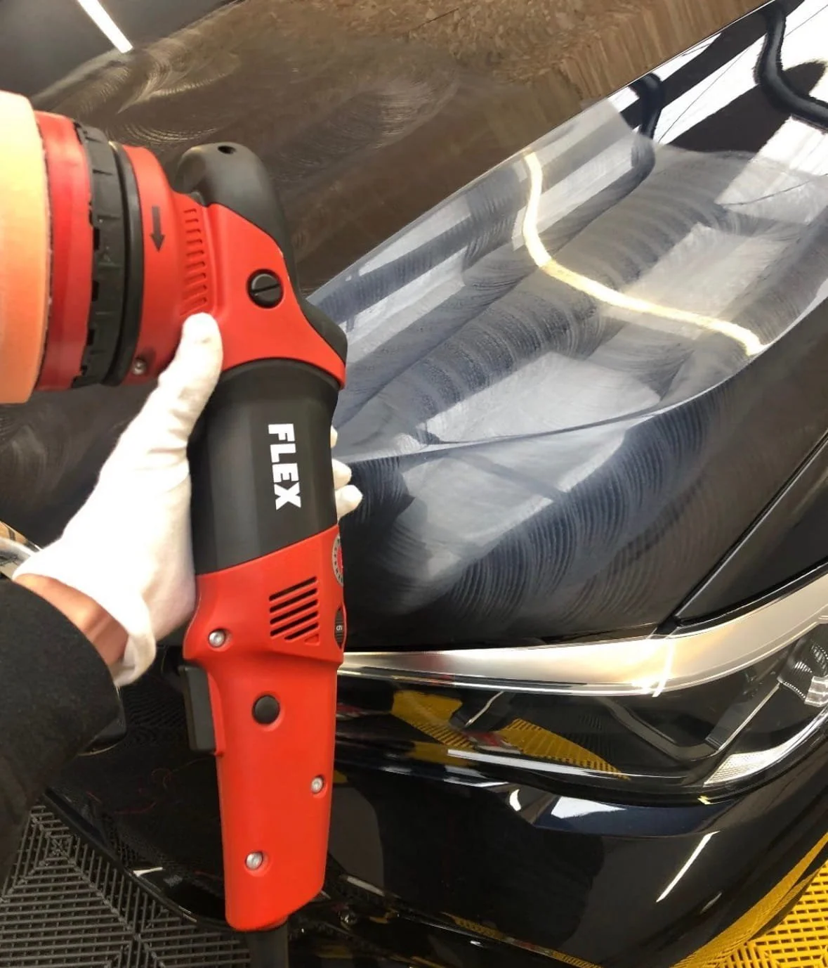 Personne utilisant une dépolisseuse pour polir la carrosserie d'une voiture.