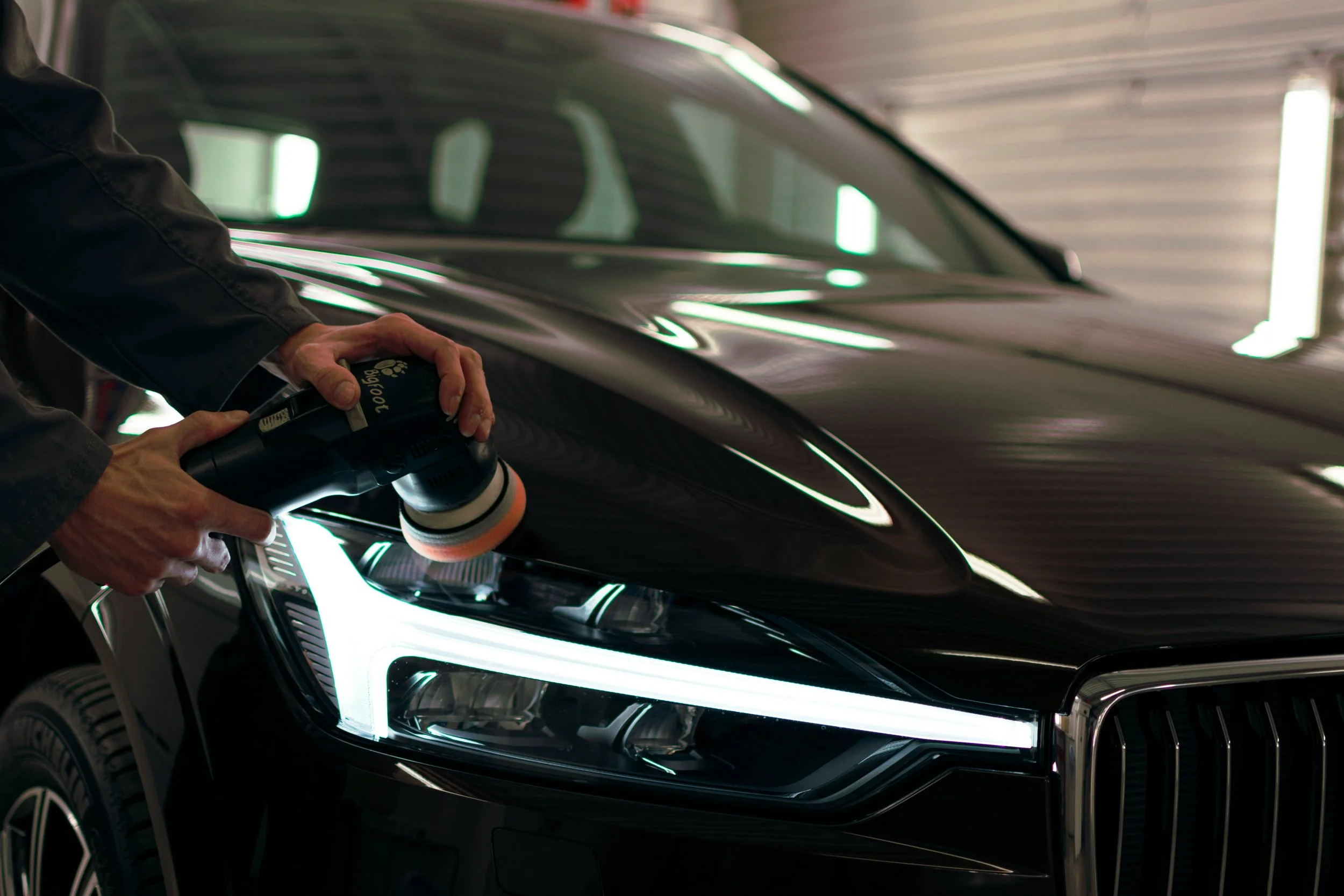 Une personne utilisant une machine à polir pour nettoyer la carrosserie d'une voiture noire dans un garage.