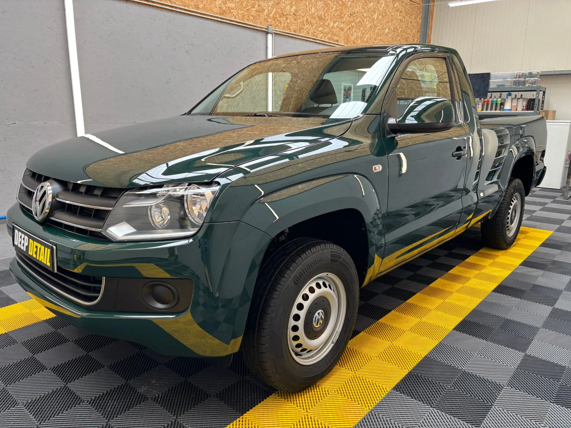 Voiture compacte verte dans un atelier, équipée pour nettoyage ou entretien, avec étagères de produits de nettoyage en arrière-plan.