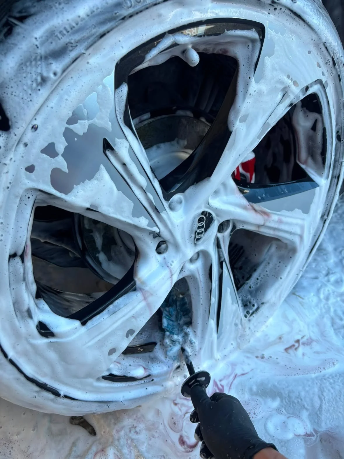 Une personne nettoie une roue de voiture en la lavant à l'eau, la roue est recouverte de mousse de savon.