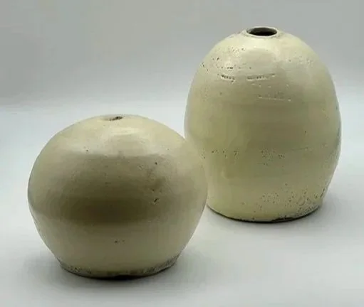 Two beige ceramic vases with smooth, rounded shapes and small openings at the top, placed on a plain surface against a light background.