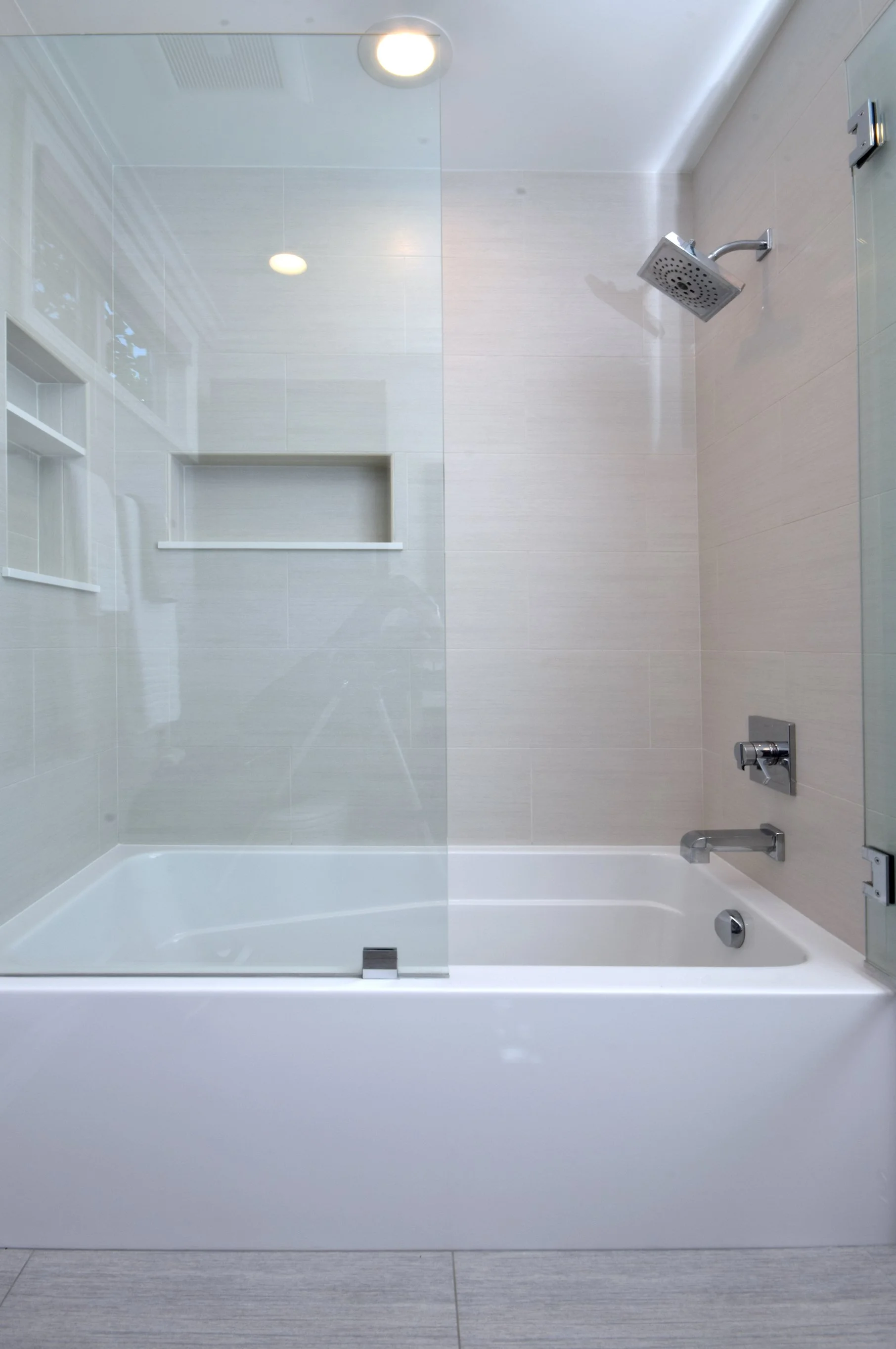 Modern bathroom shower with a glass door, rain showerhead, built-in niche, and chrome fixtures, all in light neutral tones.