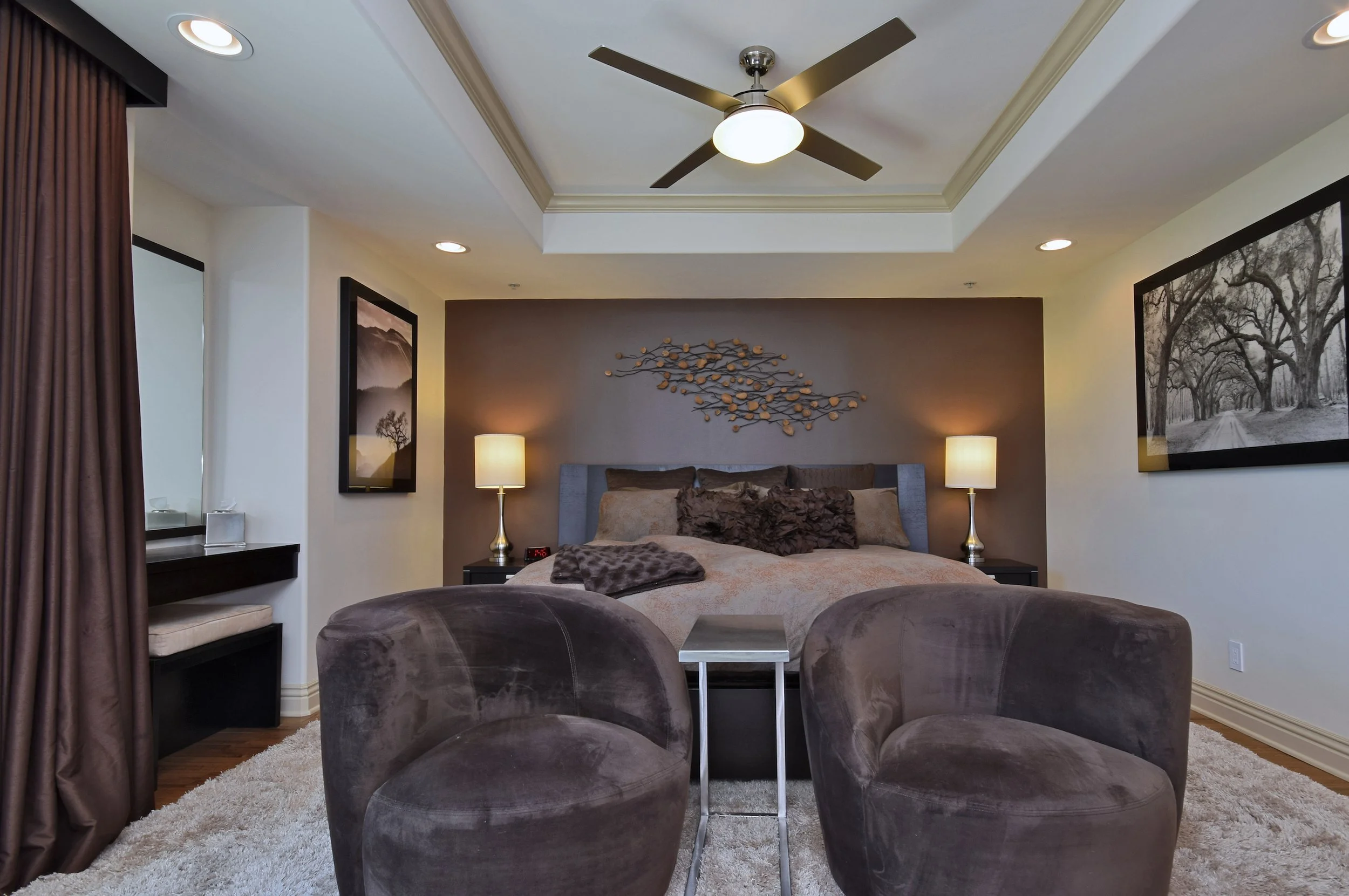 Bedroom with a bed, nightstands, table lamps, framed artwork, ceiling fan, and curtains.