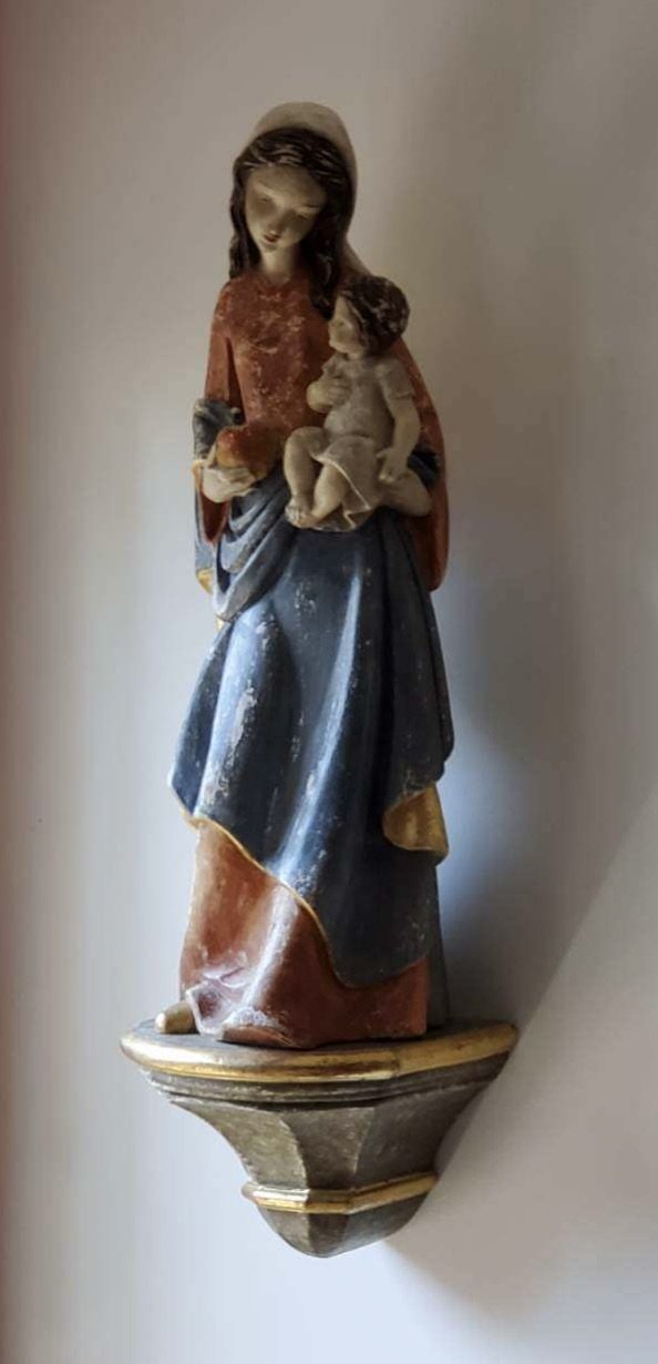A religious sculpture of a woman holding a child on a wall shelf.