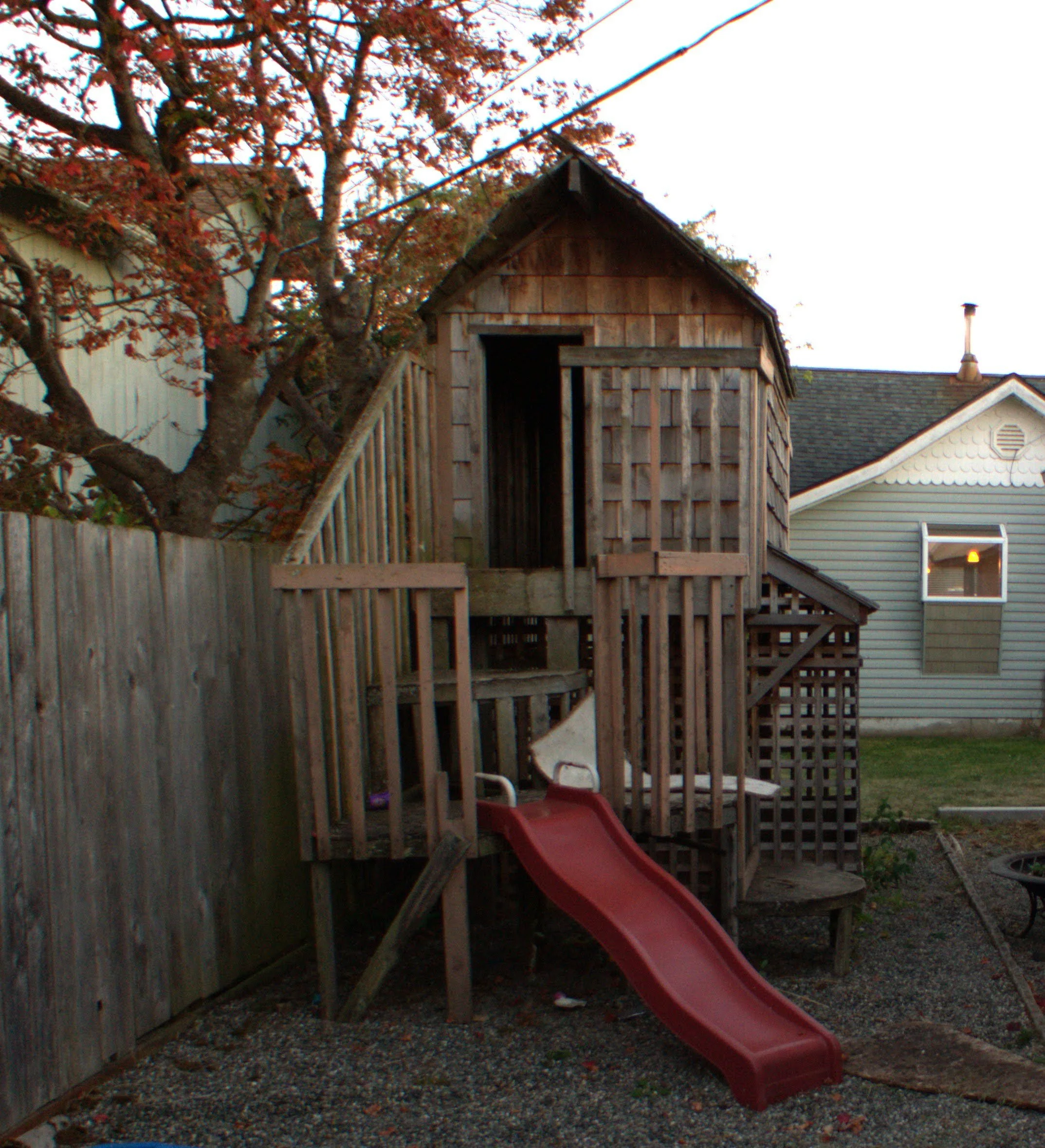 A playhouse with a wooden deck, staircase, and a red slide attached to the deck.