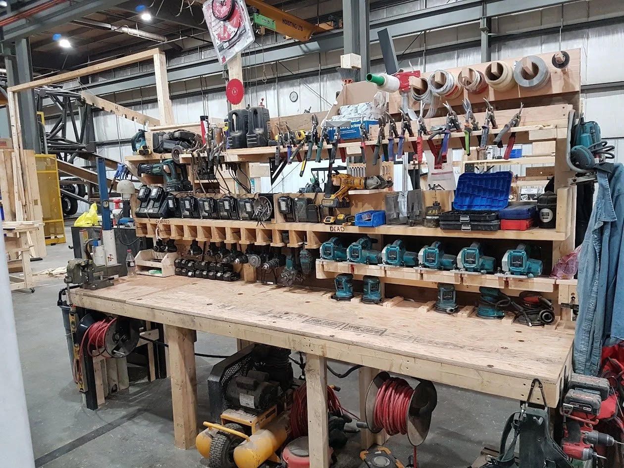 A large wooden workbench with organized tools and hardware, including drills, screwdrivers, and tapes, in a workshop.