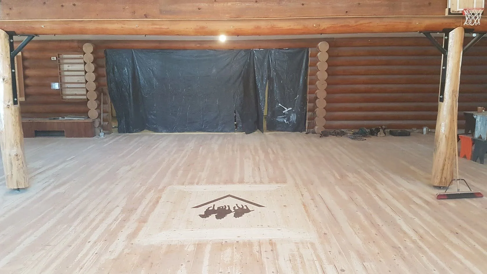 Interior of a rustic lodge or cabin with wooden walls and ceiling and wood flooring with inlay that is sanded down to refinish.