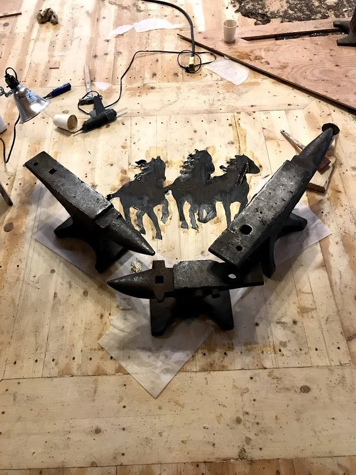 Steel anvils arranged in a semicircle on a wooden floor pressing inlay into floor while glue dries.
