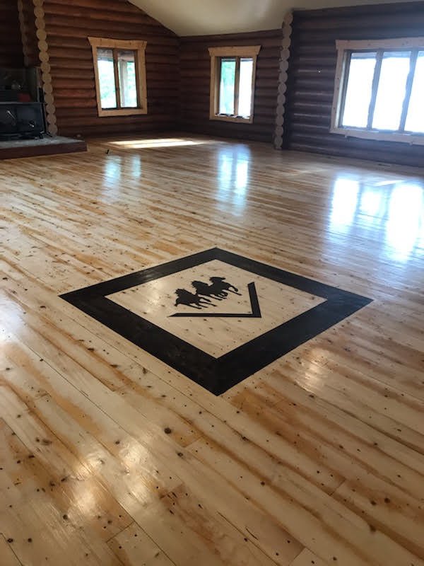 Interior of a wooden cabin with polished hardwood floors and intricate wood floor inlay depicting three running horses.