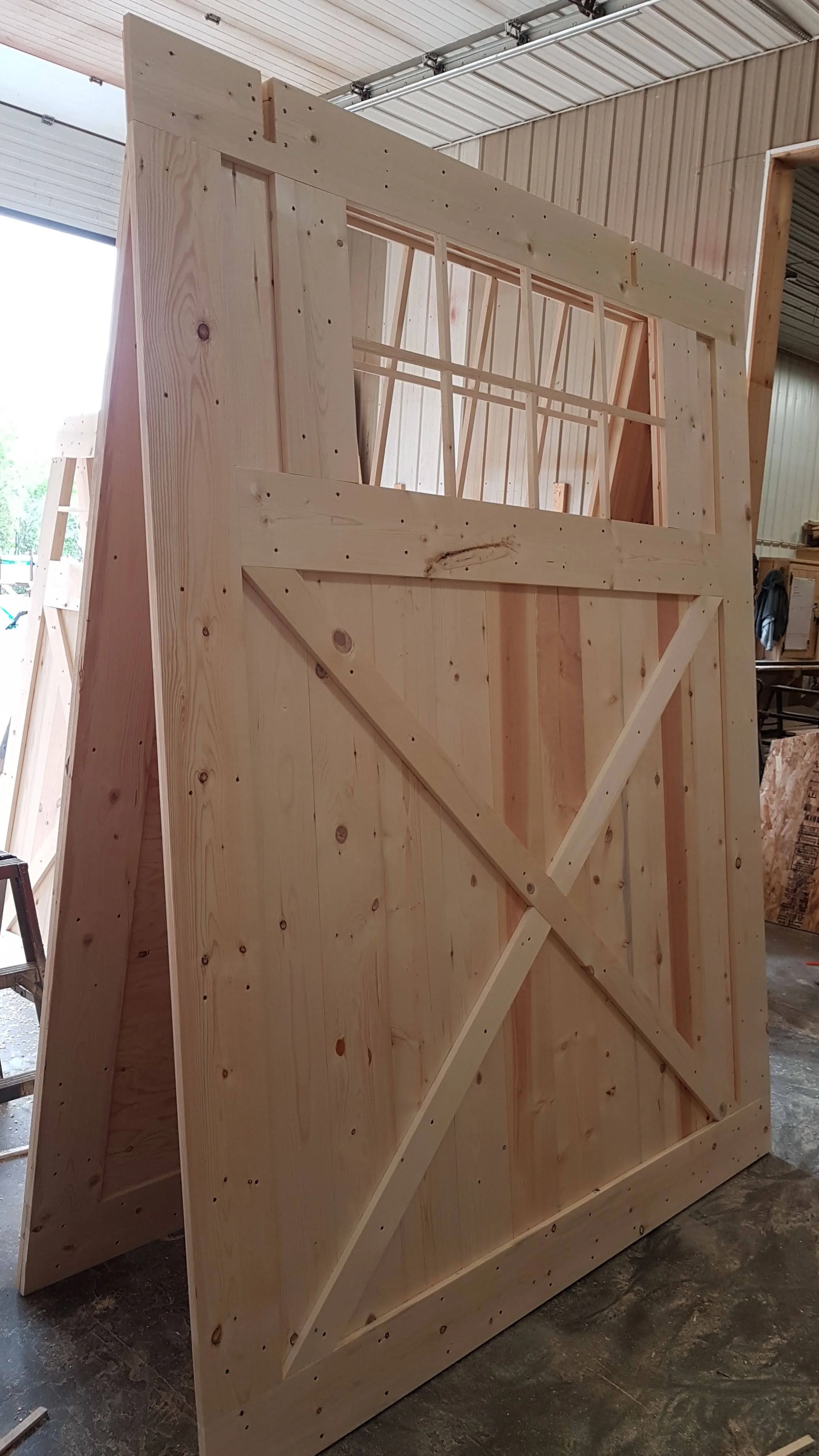Wooden barn door under construction with frame and backing panels, inside a workshop.