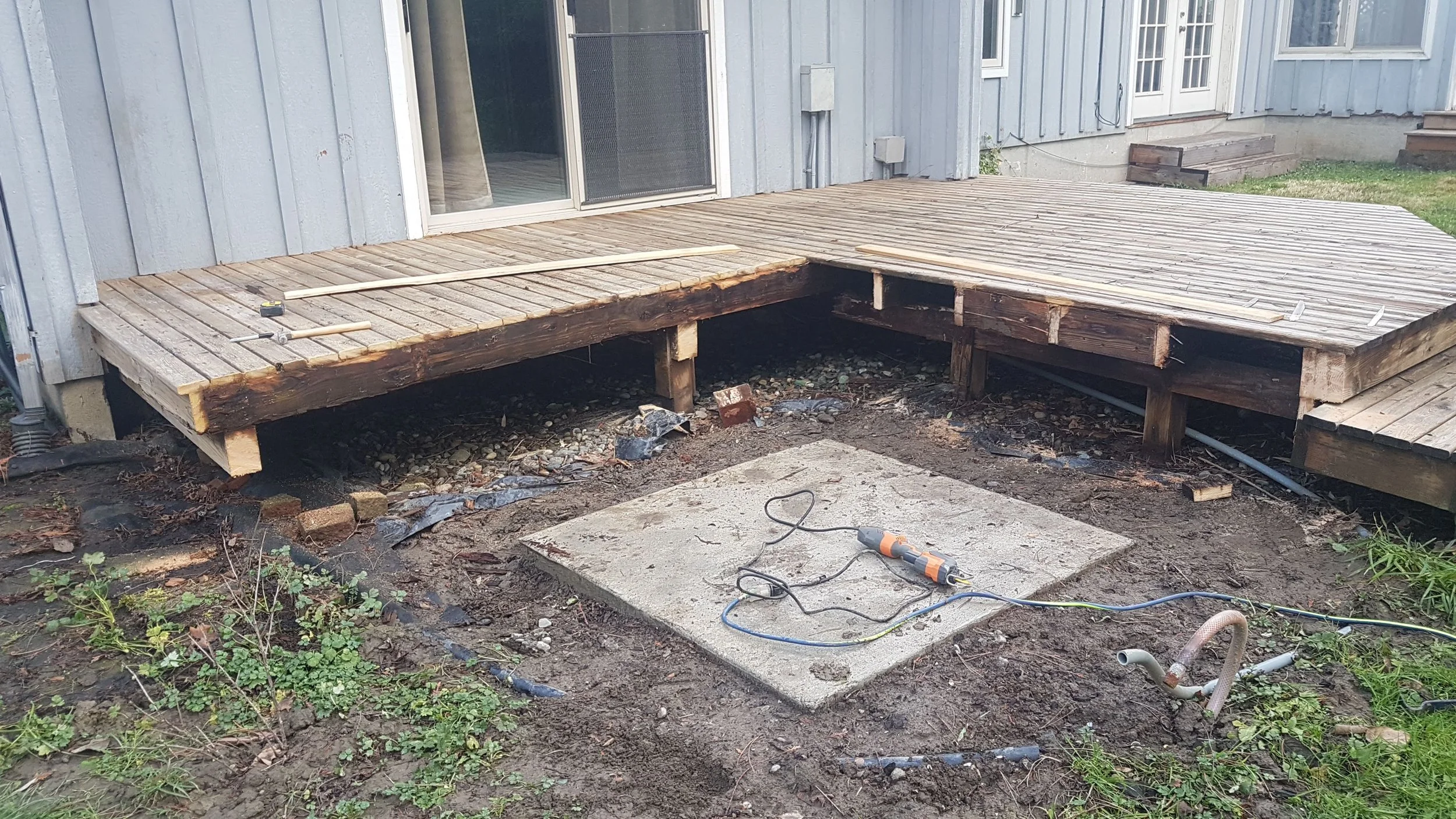 A wooden deck under construction outside a house, with tools and materials visible, and the area underneath exposed.
