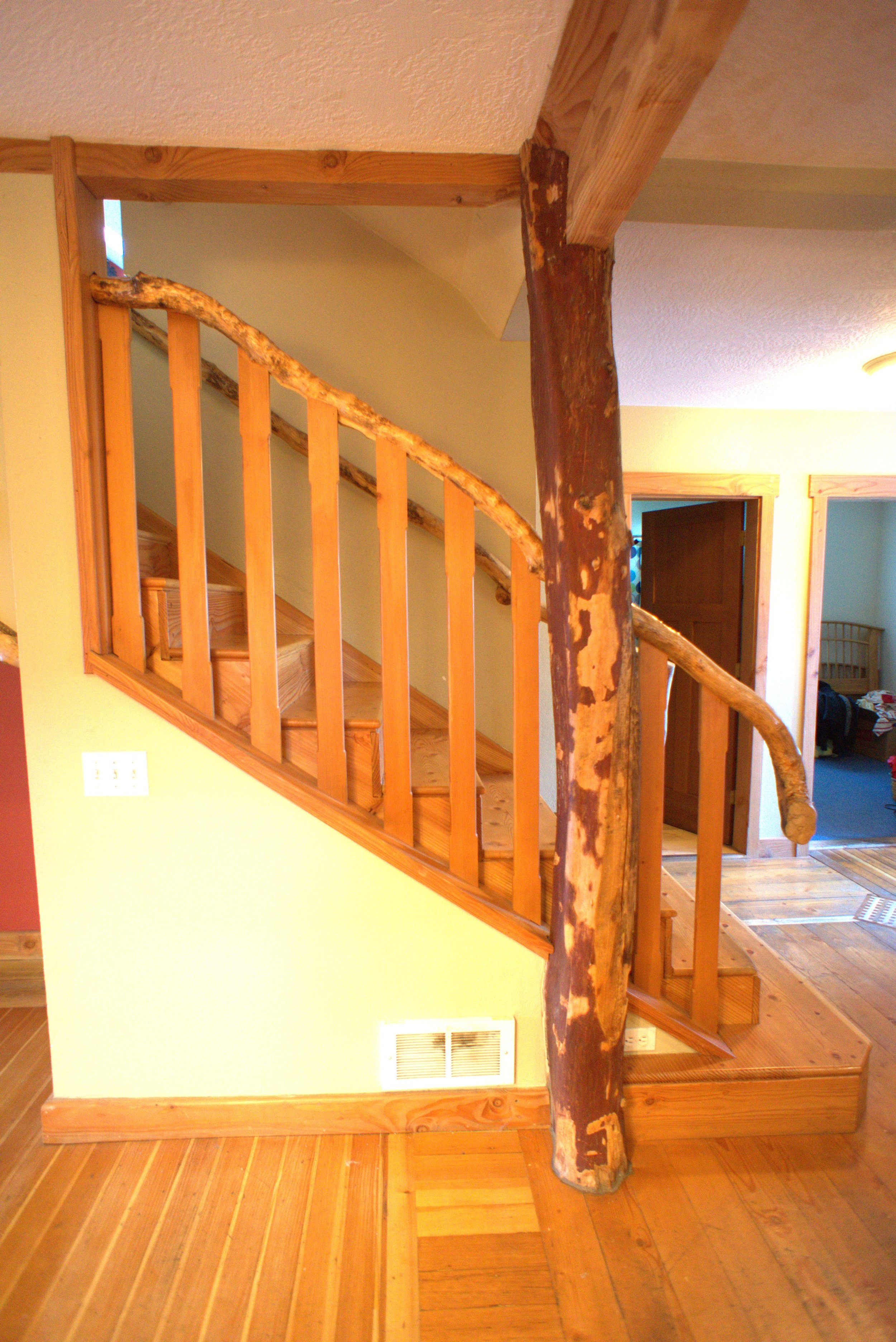 Interior view of a staircase with wooden railings, a natural wood banister, a log post, and wooden flooring.